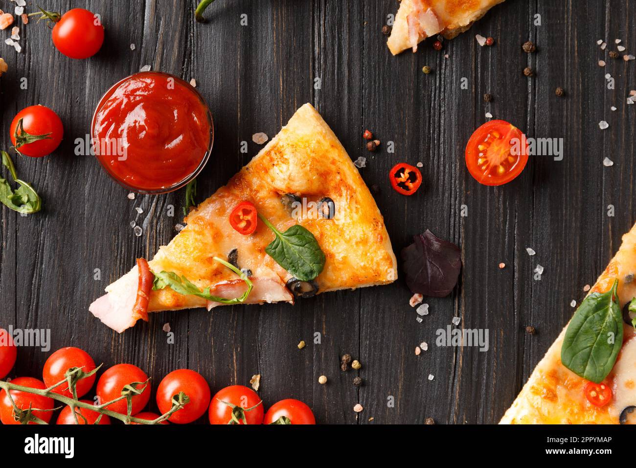 Des tranches de pizza avec des jerky, des olives, du fromage et des herbes sont disposées sur un fond en bois foncé, une branche de tomates cerises fraîches, des sauces Banque D'Images