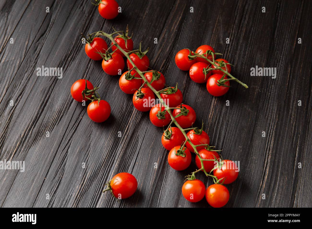 Tomates cerises sur une branche sur fond de bois foncé vue du dessus. Tomates cerises fraîches sur fond de bois. Une alimentation saine. Véganisme. Banque D'Images
