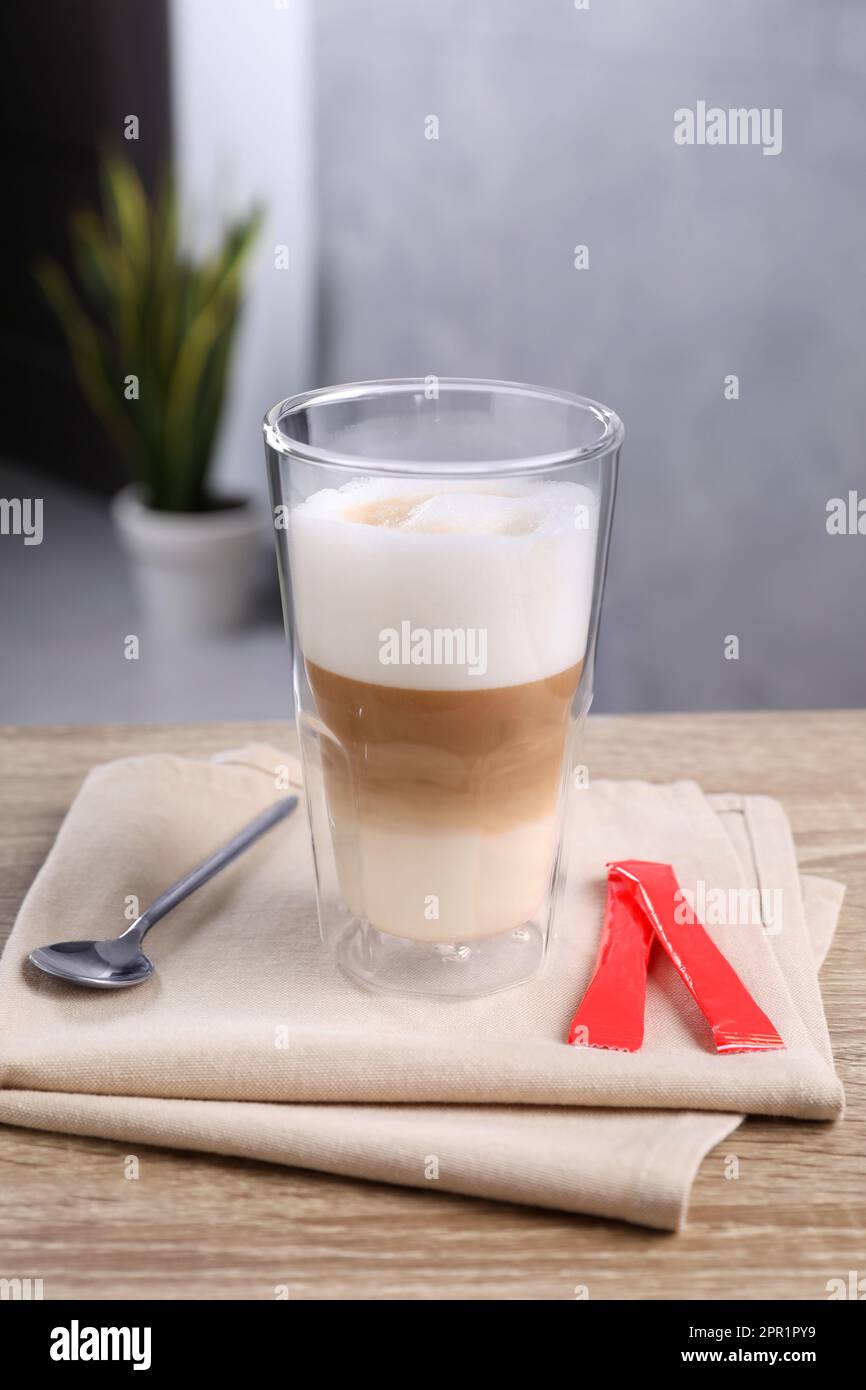 Délicieux café en verre et sachets de sucre sur une table en bois Banque D'Images