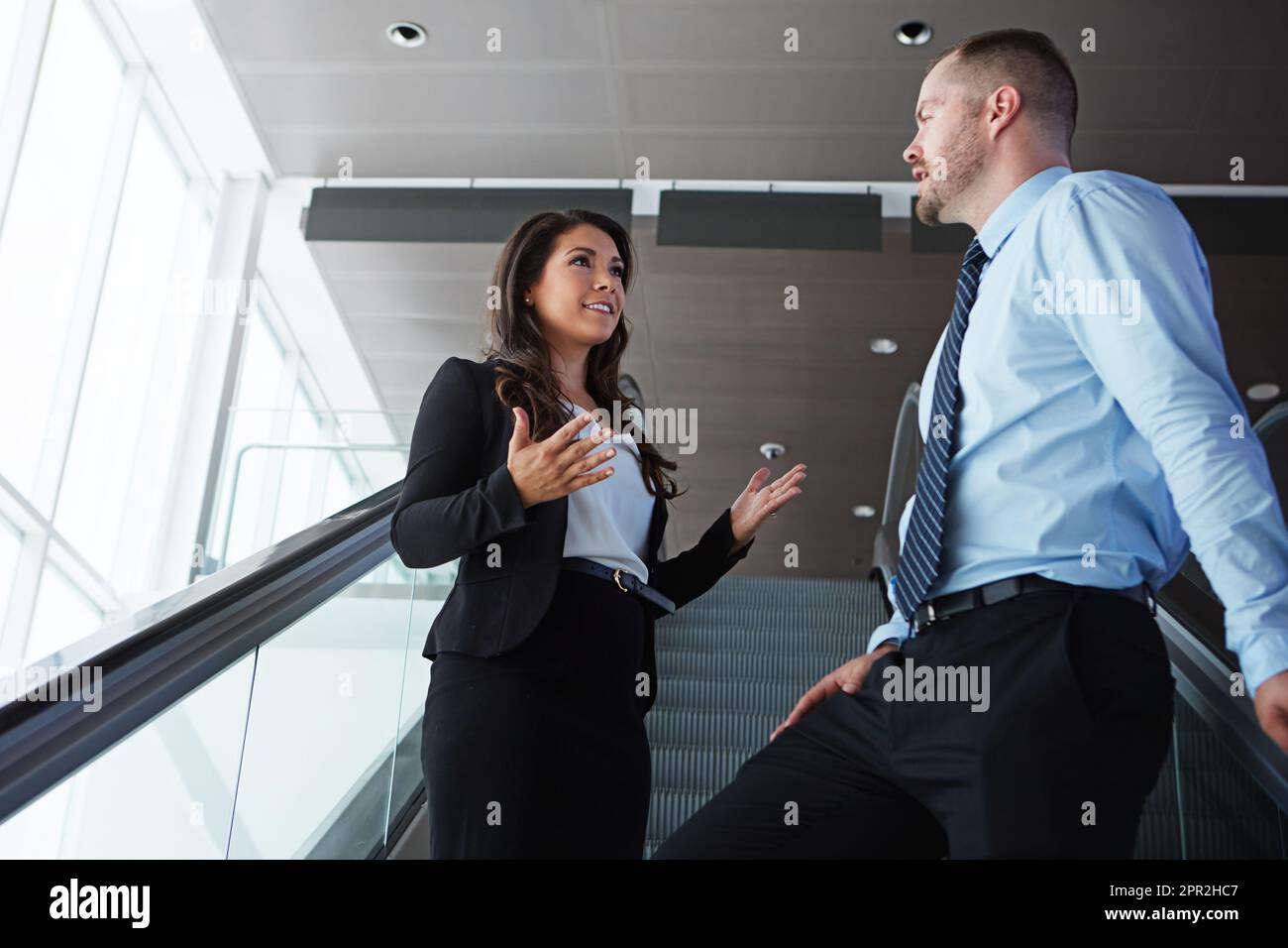 Parler d'affaires avant qu'ils n'embarque. deux associés d'affaires ayant une conversation en descendant un escalier roulant dans un aéroport. Banque D'Images