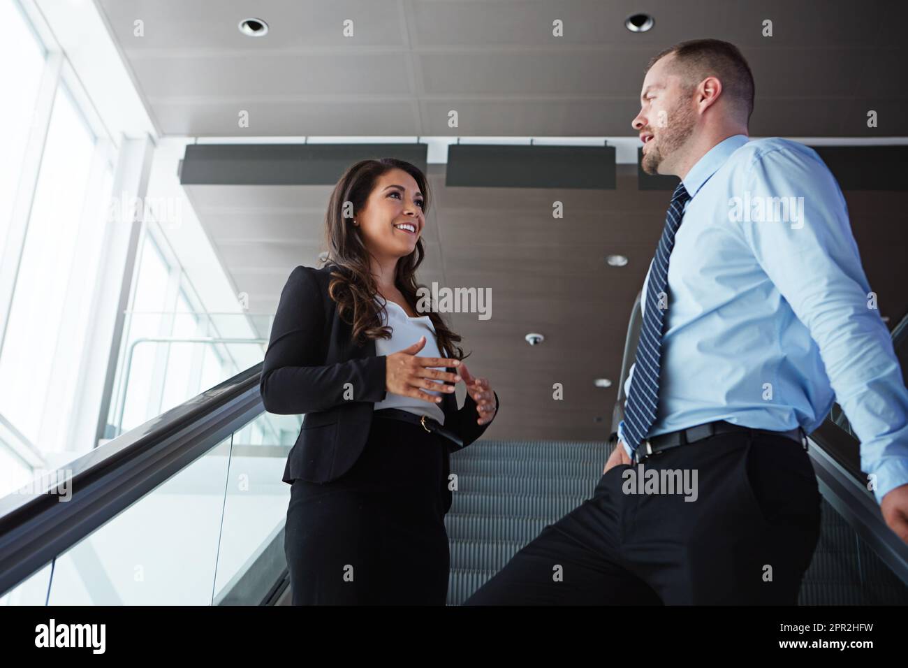 Prendre soin de ses affaires avant de prendre le vol. deux associés d'affaires ayant une conversation en descendant un escalier roulant dans un aéroport. Banque D'Images