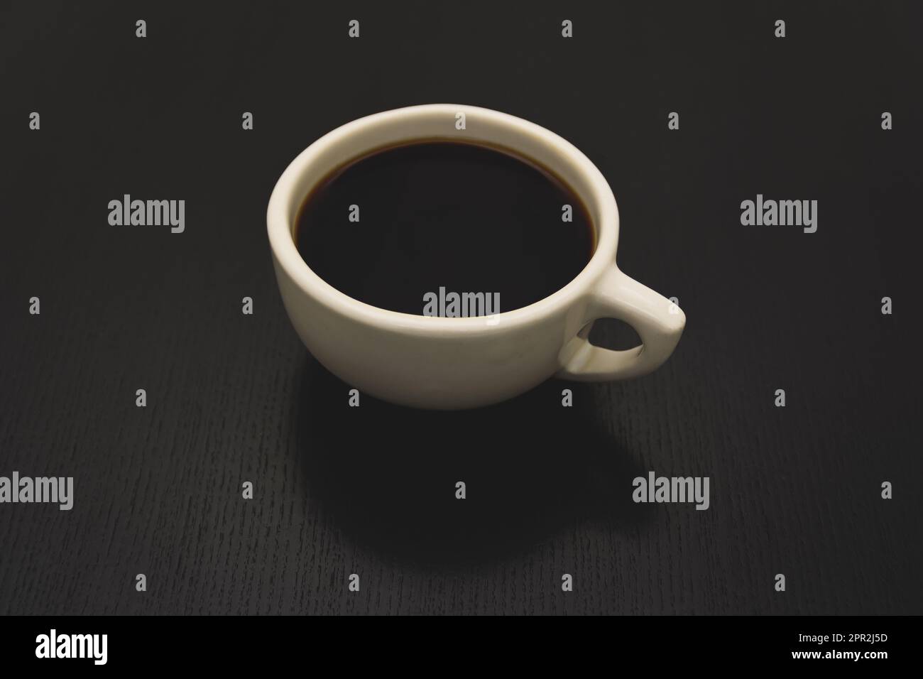 Un café noir dans une tasse blanche classique de style américain est posé sur une table noire. Banque D'Images