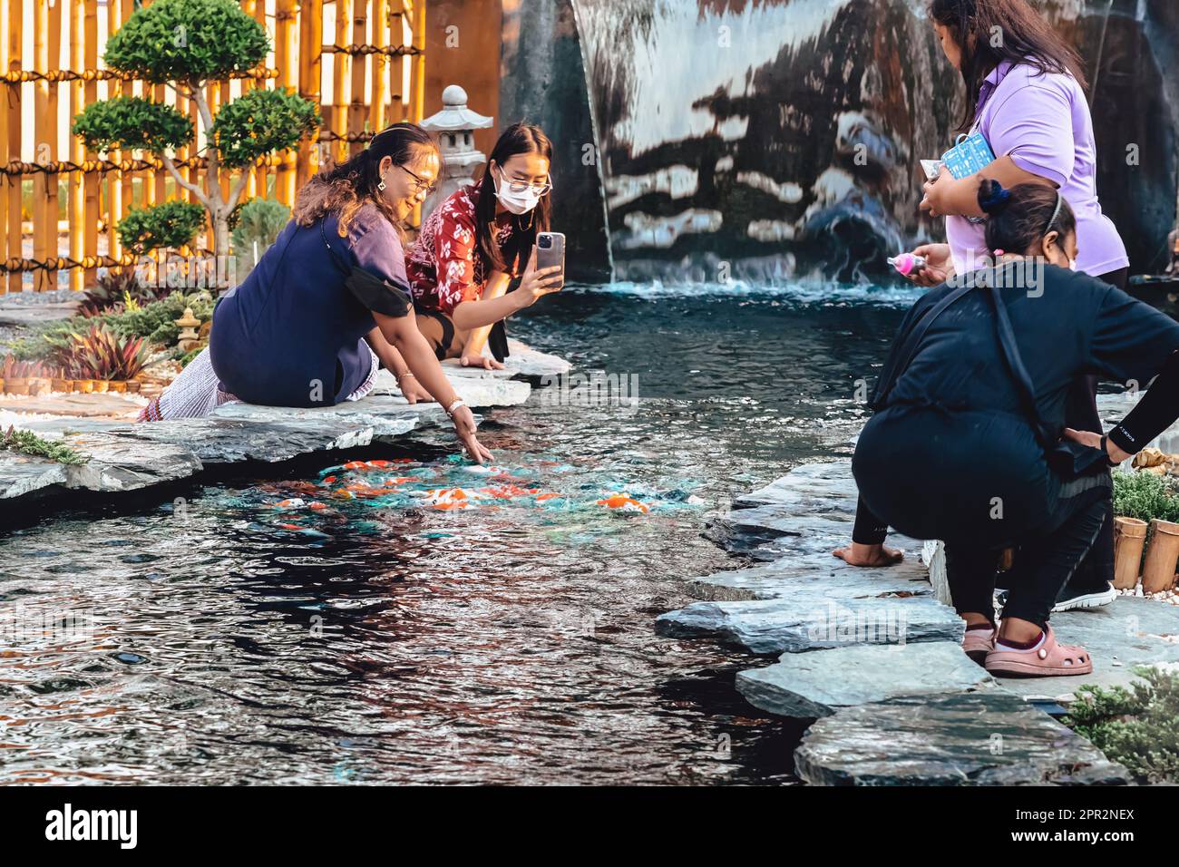 KANCHANABURI -THAÏLANDE, 30 MARS 2023 : touristes non identifiés viennent visiter et nourrir koi ou carpe fantaisie dans un petit étang avec beau jardin décoré Banque D'Images