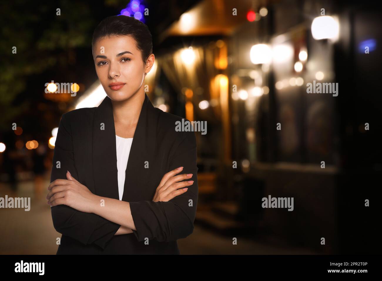 Portrait de l'hôtesse en uniforme et vue floue du café avec terrasse extérieure la nuit. Espace pour le texte Banque D'Images