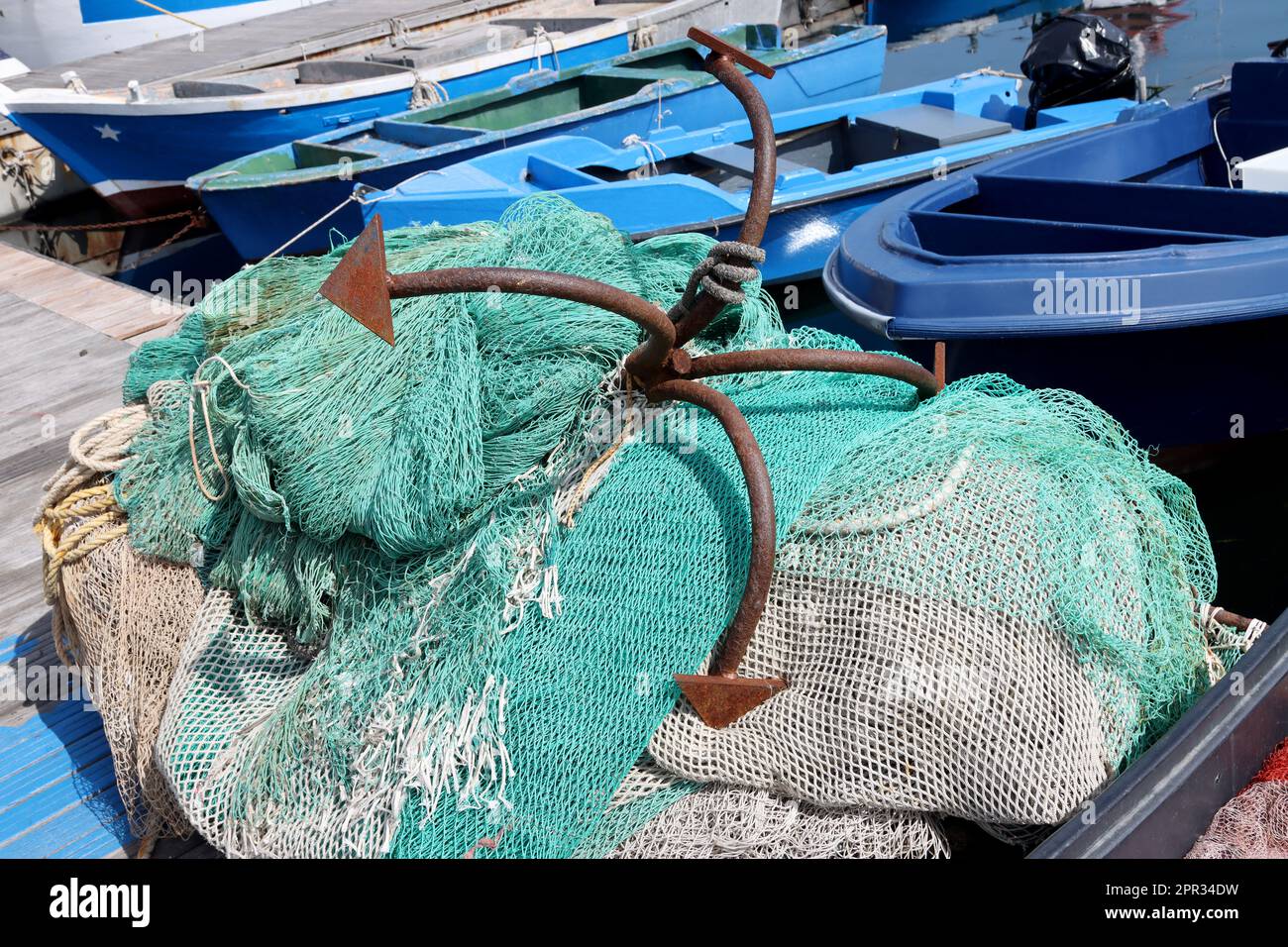 Ancienne ancre rouillée sur un tas de filets de pêche avec des bateaux de pêche en arrière-plan Banque D'Images