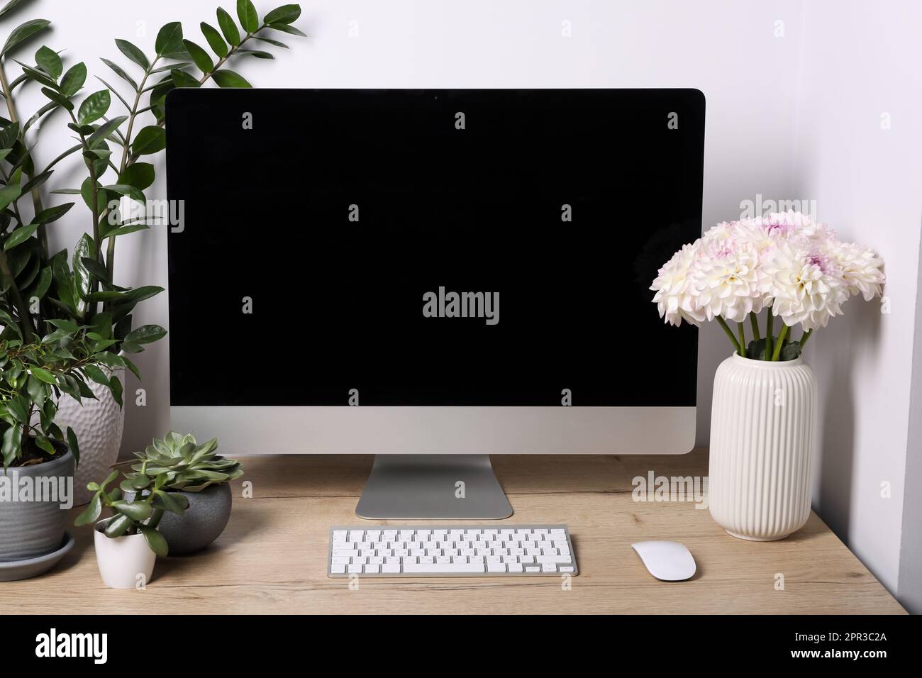 Espace de travail confortable avec ordinateur moderne, plantes vertes et belles fleurs sur table en bois à l'intérieur Banque D'Images