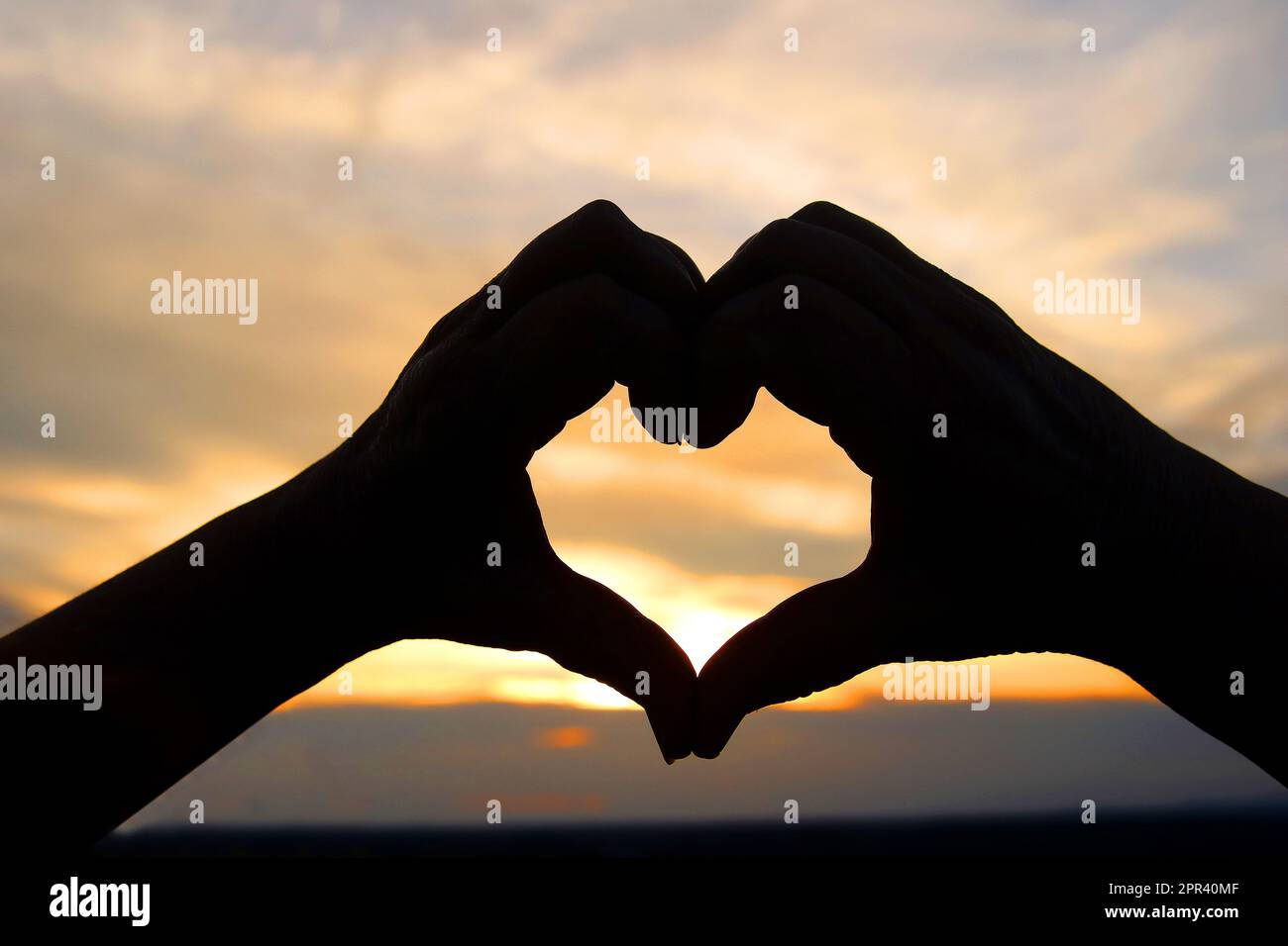 mains formant un coeur devant un coucher de soleil romantiv Banque D'Images