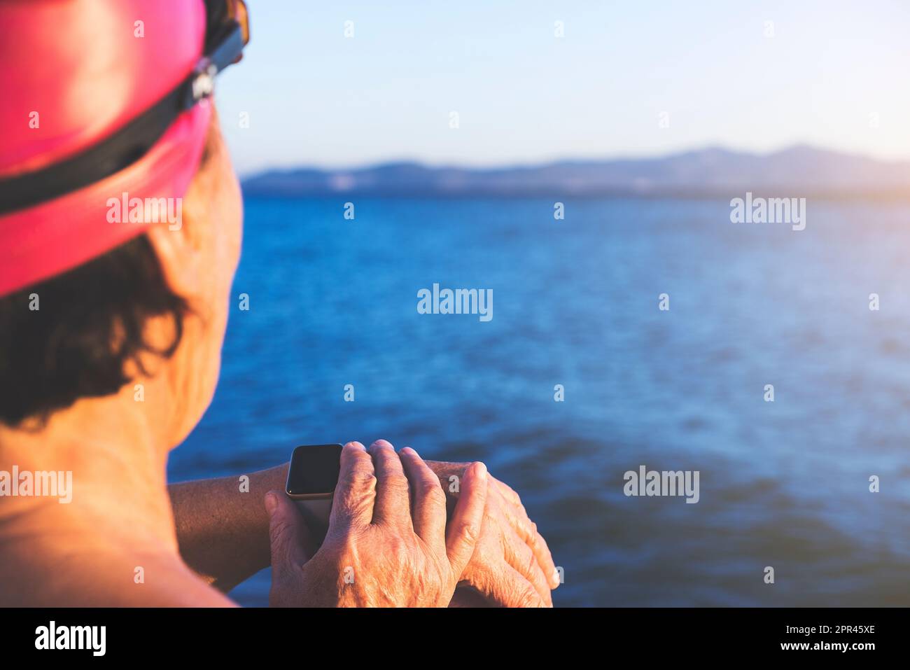 Photo arrière d'une femme âgée à la plage, debout au bord de la mer. Porter  un maillot de bain bleu, prêt à nager. Utilisation de la montre  intelligente au poignet Photo Stock -