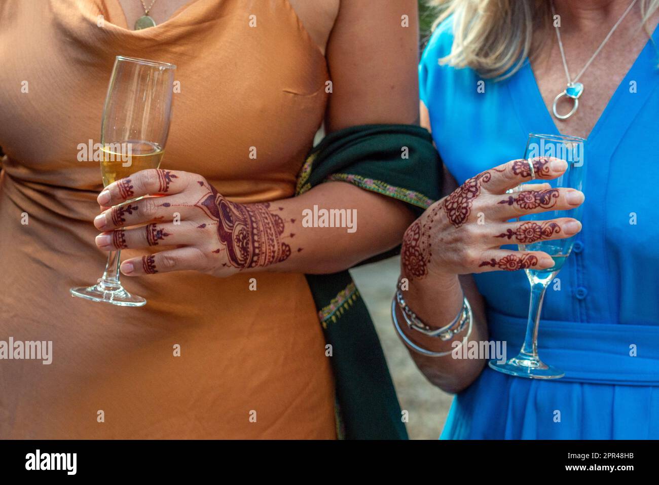 Gros plan de deux femmes tenant des verres à vin, avec des motifs d'art corporel Henna (Lawsonia inermis) sur leur peau. Banque D'Images