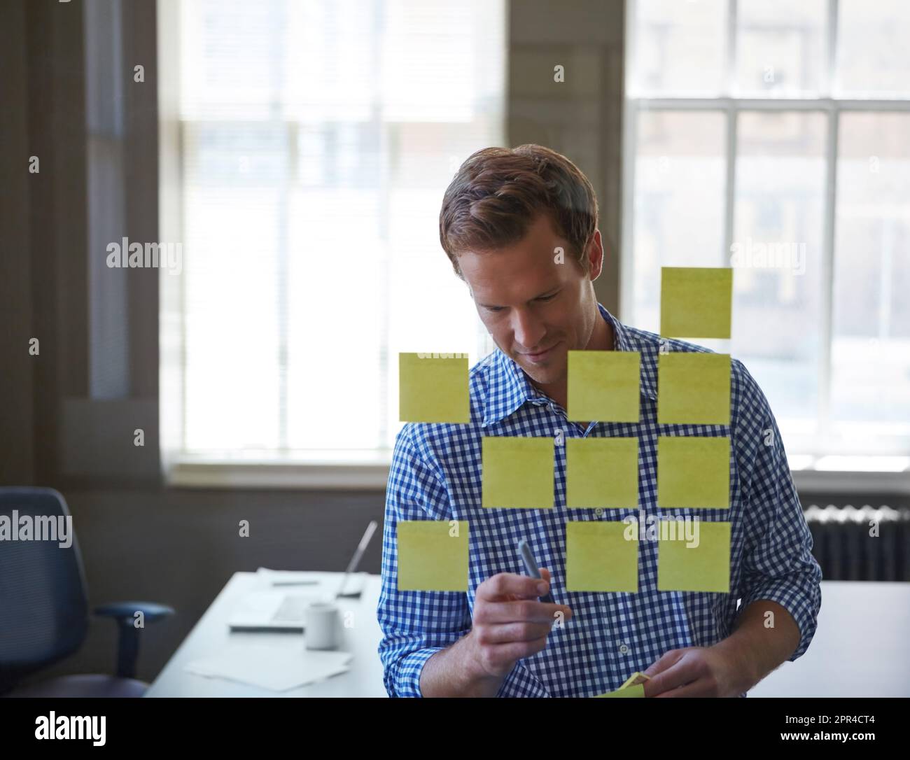 Ce sont les petites choses qui créent de grandes entreprises. un beau homme d'affaires qui organise des notes adhésives sur un panneau en verre. Banque D'Images