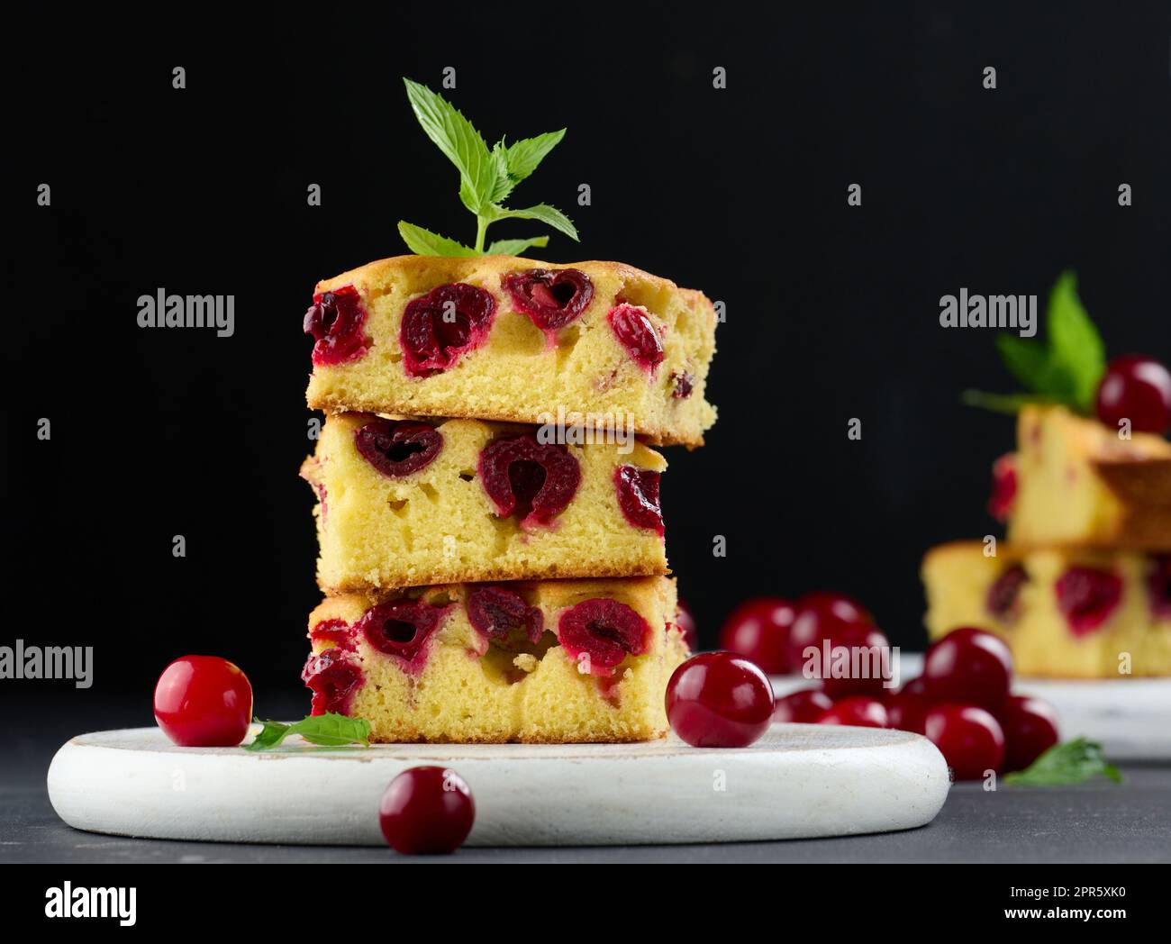Morceaux de gâteau de Savoie cuits avec des cerises mûres rouges sur un panneau de bois blanc Banque D'Images