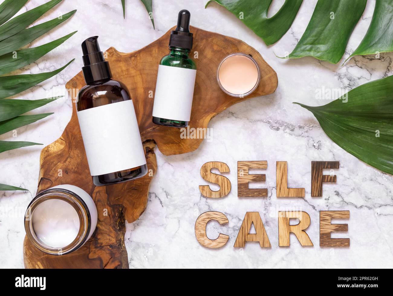 Texte Self Care près des bouteilles de cosmétiques et des feuilles de monstère vue du dessus, maquette Banque D'Images