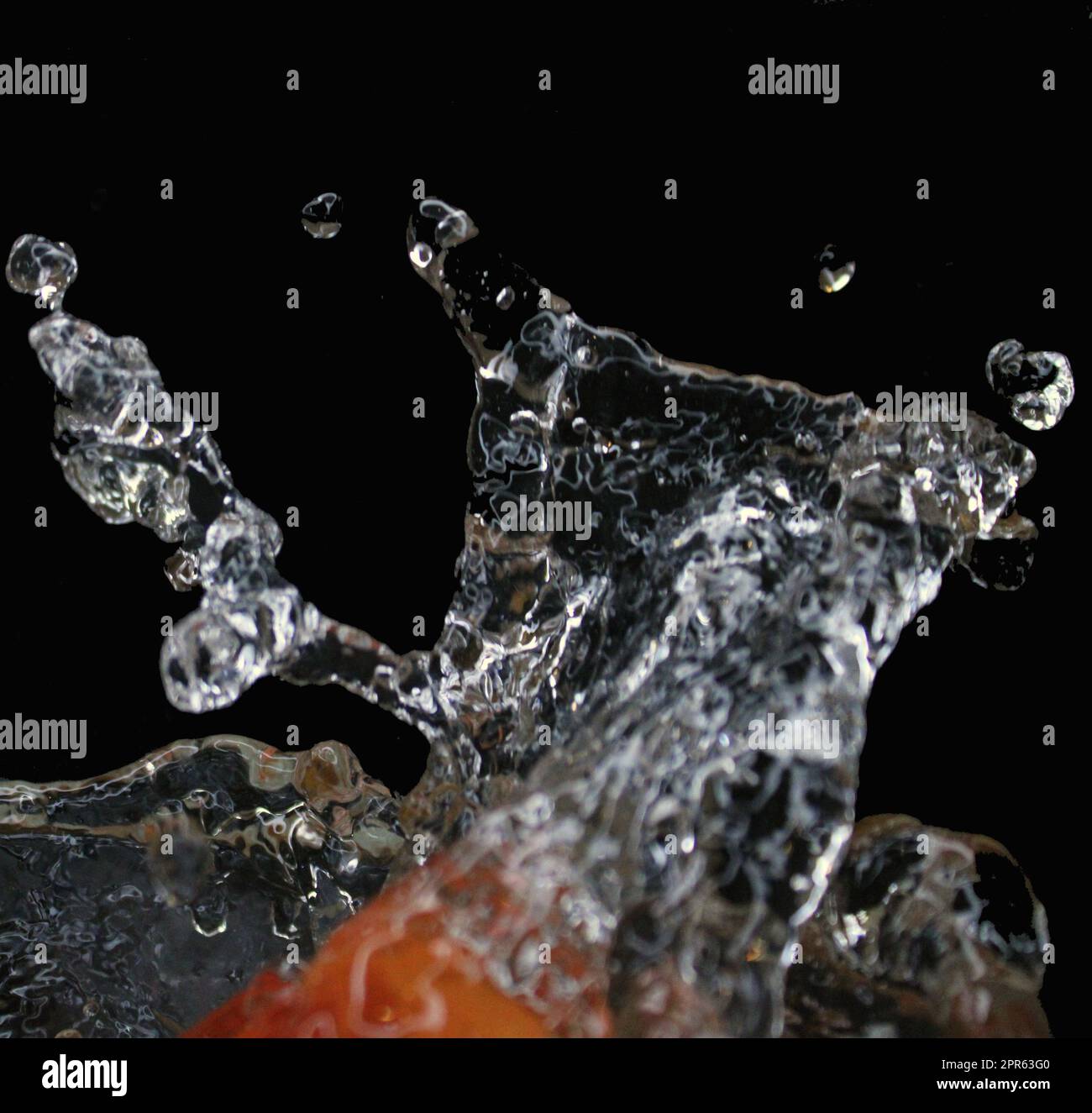 Éclaboussures d'eau isolées sur fond noir. Le fruit tombe dans l'eau. Banque D'Images