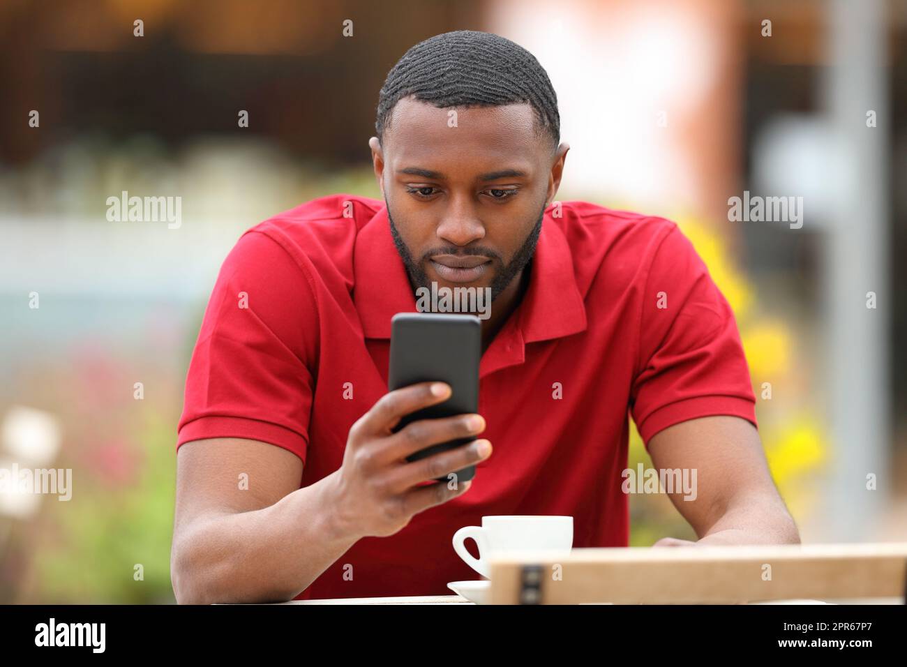 Homme noir sérieux utilisant un téléphone cellulaire dans une terrasse de bar Banque D'Images