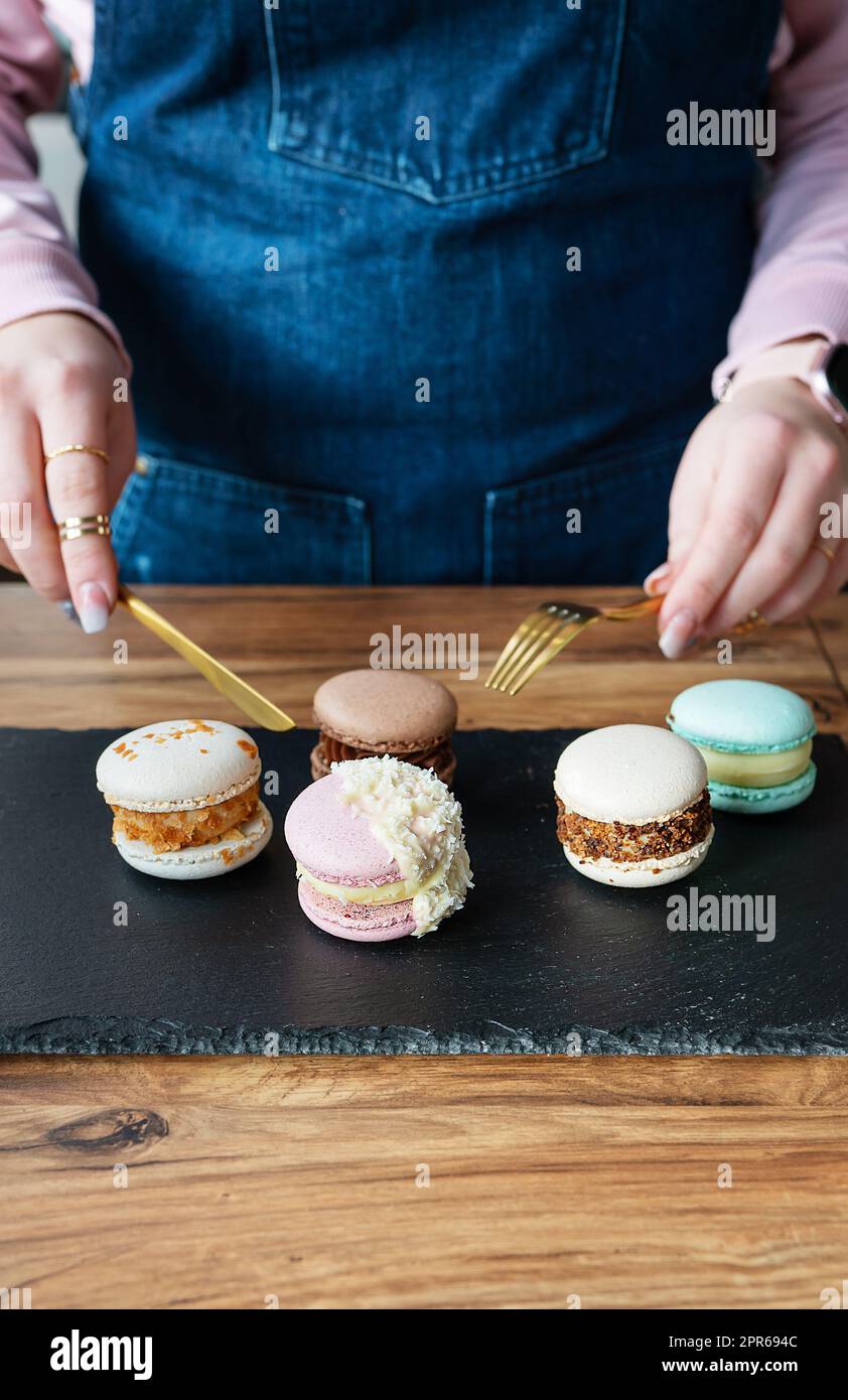 Un délicieux dessert de pâtes - une pâtisserie française douce se trouve sur un stand noir en béton et une fille avec un couteau et une fourchette coupe des bonbons. Banque D'Images