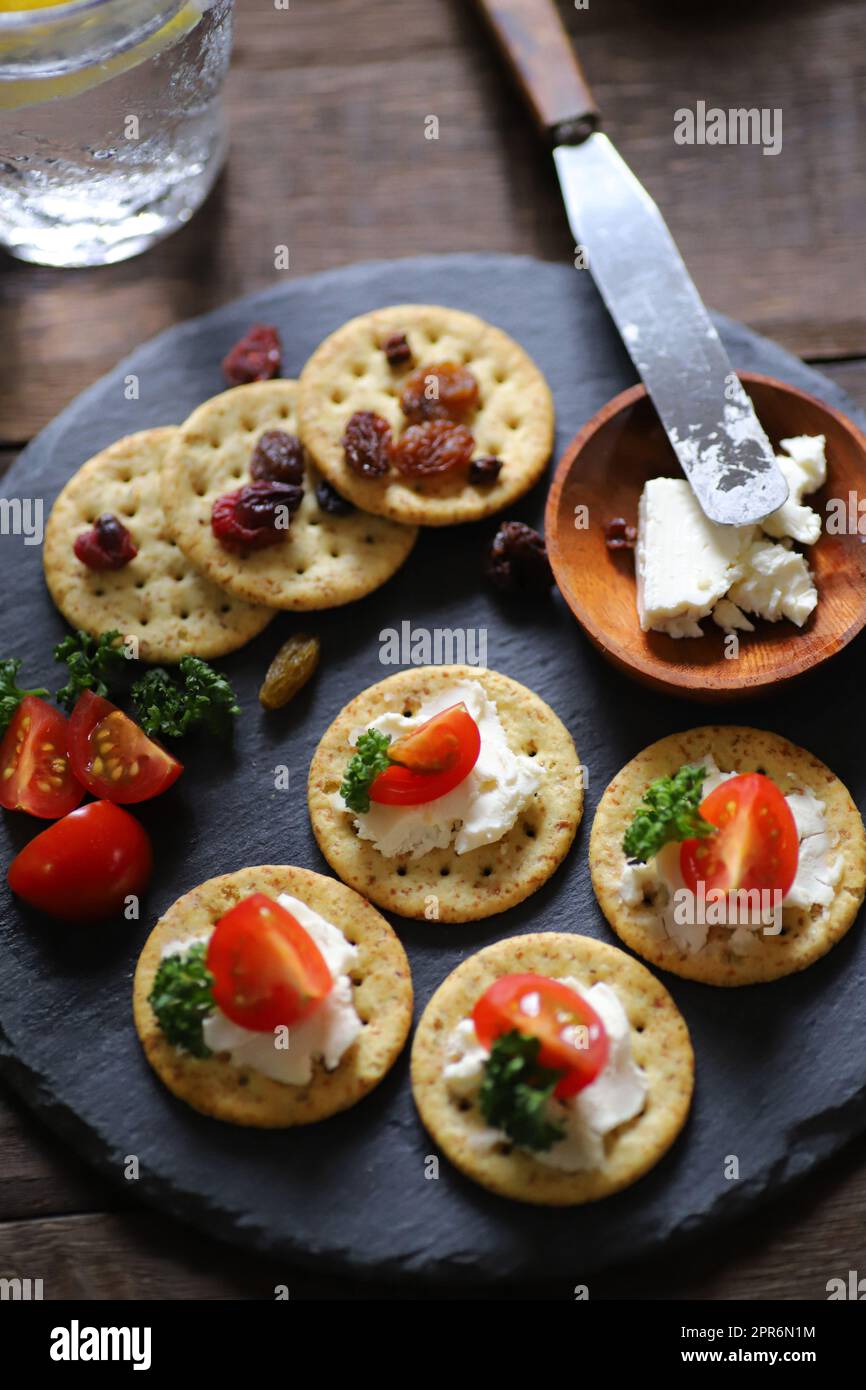 Un verre rempli de soda au whisky et de hors-d'œuvre (craquelins, fruits secs, tomates, persil et fromage à la crème) Banque D'Images