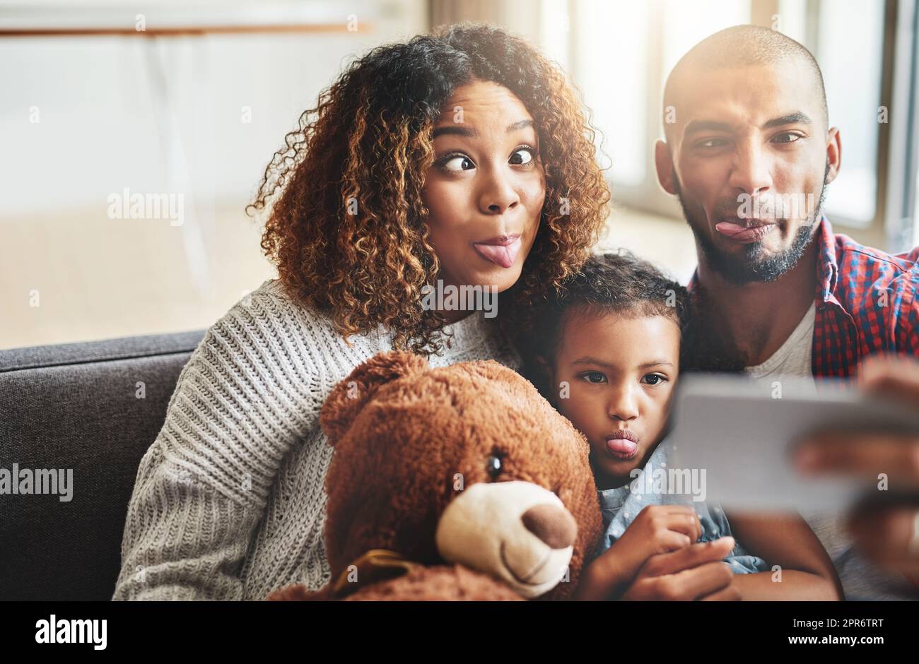 Ce n'est pas un temps de qualité jusqu'à ce que quelqu'un prenne un selfie. Photo d'une adorable petite fille prenant des selfies avec ses parents à la maison sur un téléphone portable. Banque D'Images