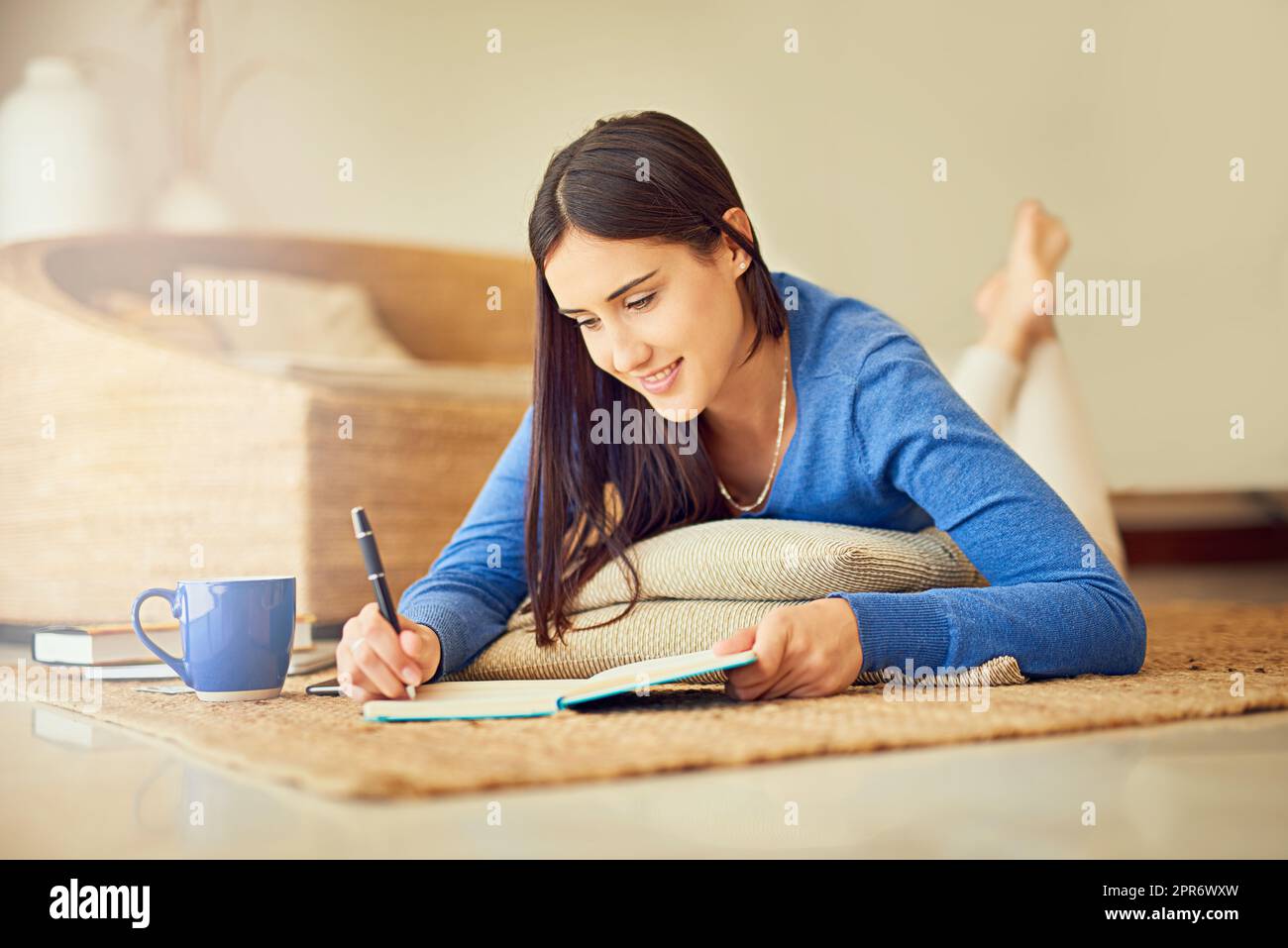 Juste en pennant quelques pensées. Photo d'une jeune femme heureuse prenant des notes dans son carnet tout en étant couché sur son sol de salon. Banque D'Images