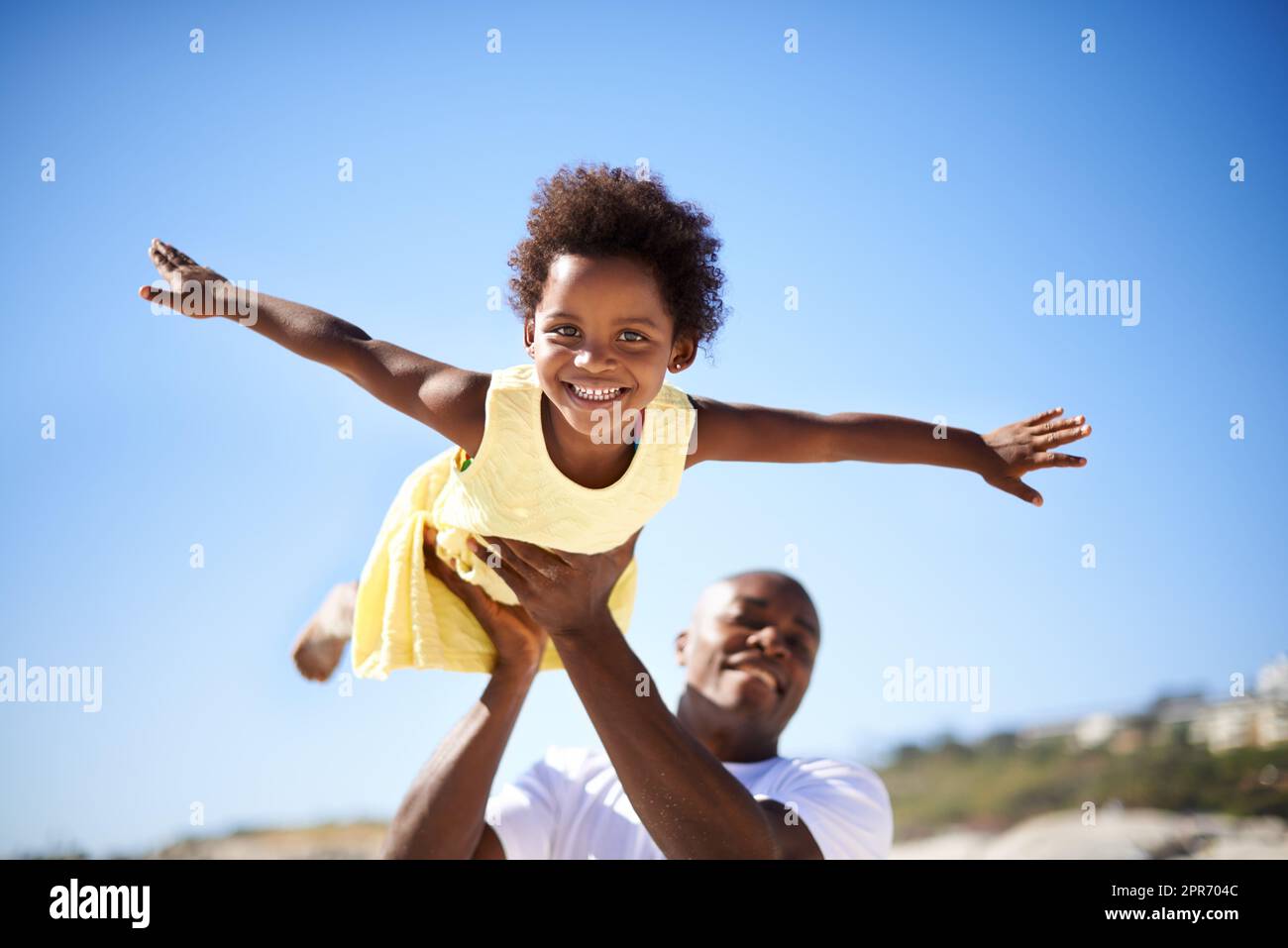 Aider sa fille à monter en flèche. Un père soulevant son adorable fille dans l'air tout en appréciant une journée à la plage. Banque D'Images