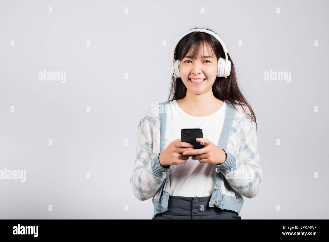 Une femme se réjouit de sourire en écoutant de la radio musicale dans un casque bluetooth et en tenant le téléphone Banque D'Images