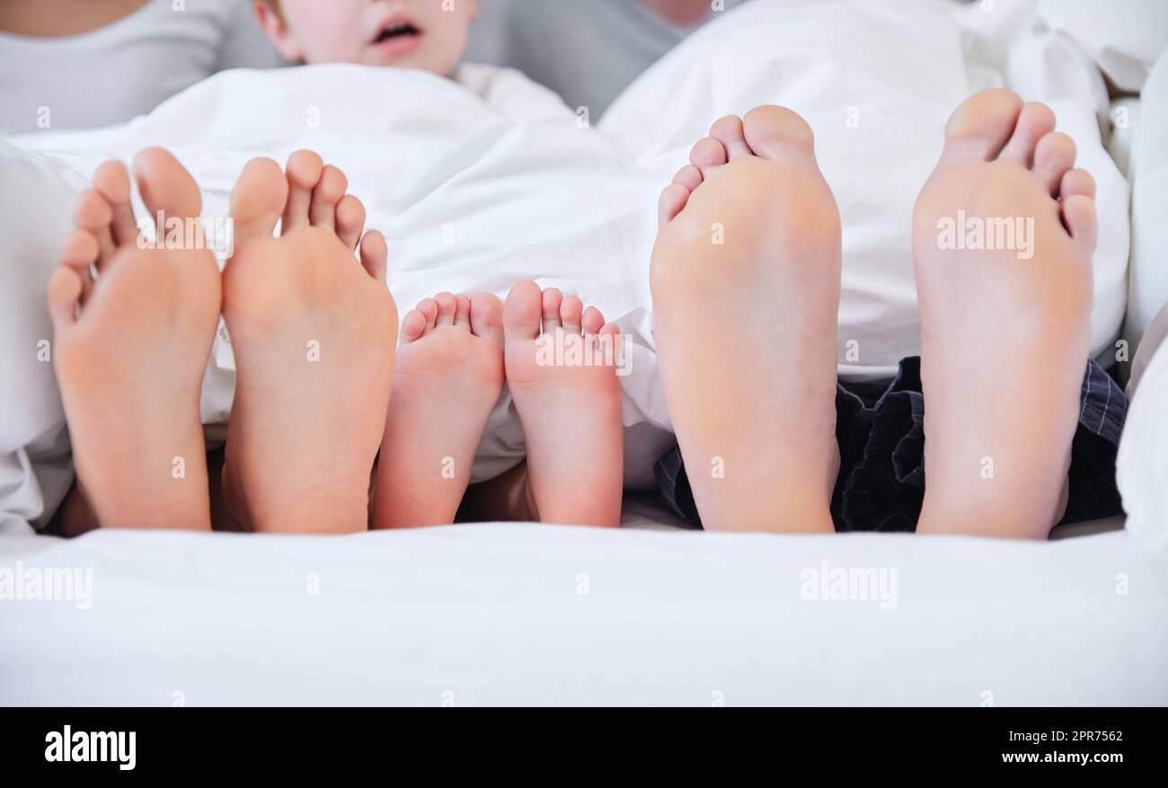 Journée de repos en famille. Prise de vue d'une famille méconnue qui s'est posée pieds nus sur un lit à la maison. Banque D'Images