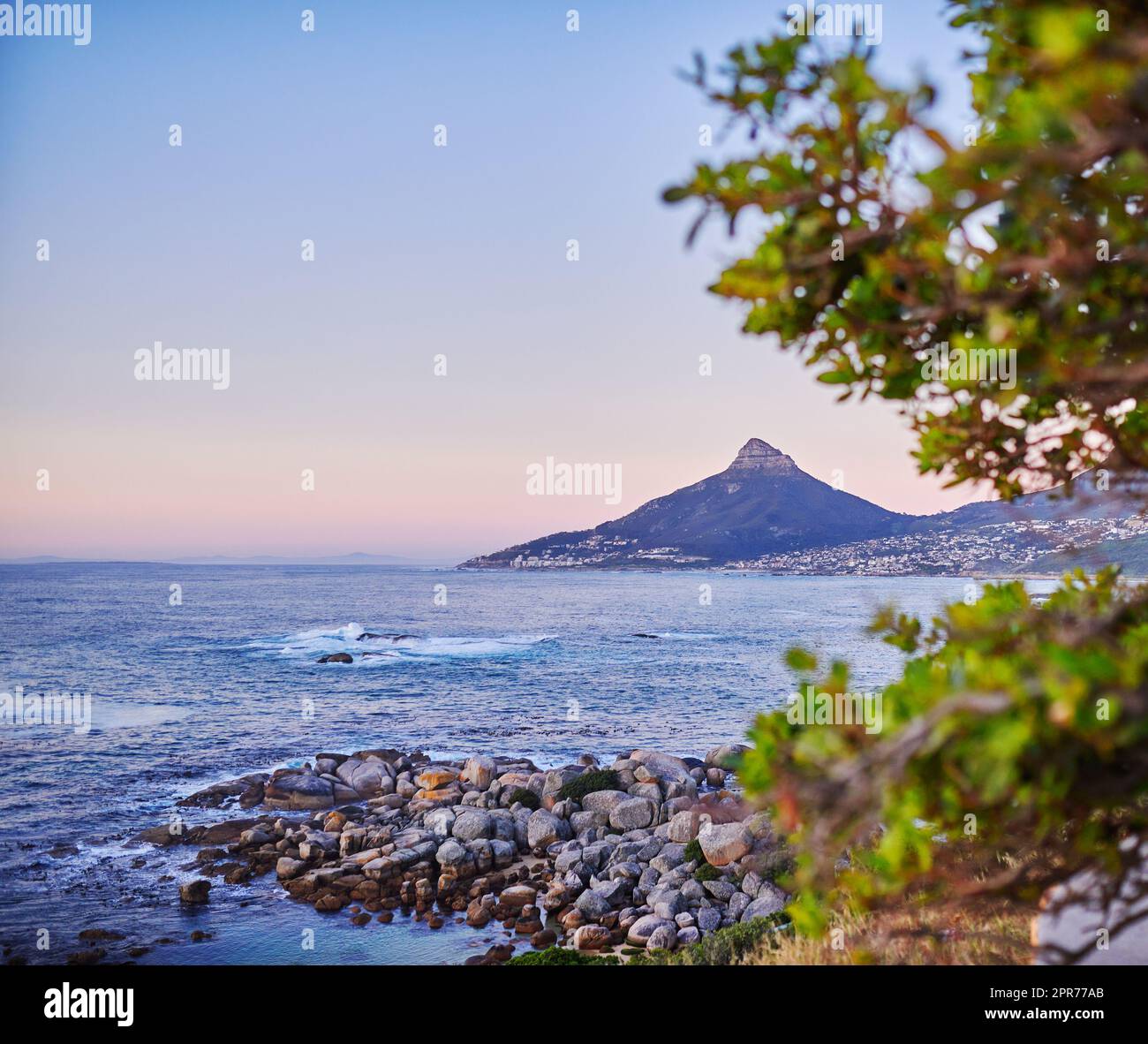 Vue sur l'océan sur un rivage rocheux peu profond avec Lions Head, parc national de Table Mountain au Cap, Afrique du Sud en arrière-plan. Calme plage calme pendant le coucher du soleil sur une belle soirée d'été Banque D'Images