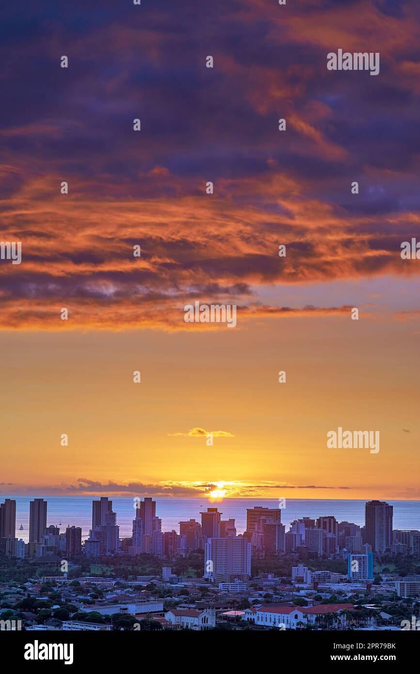 Un coucher de soleil sur un horizon de la ville près de la mer avec ciel nuageux violet et orange. Lever de soleil sur un horizon bleu près d'un paysage urbain avec espace de copie. Destination de vacances paisible la nuit à Waikiki, Hawaï Banque D'Images