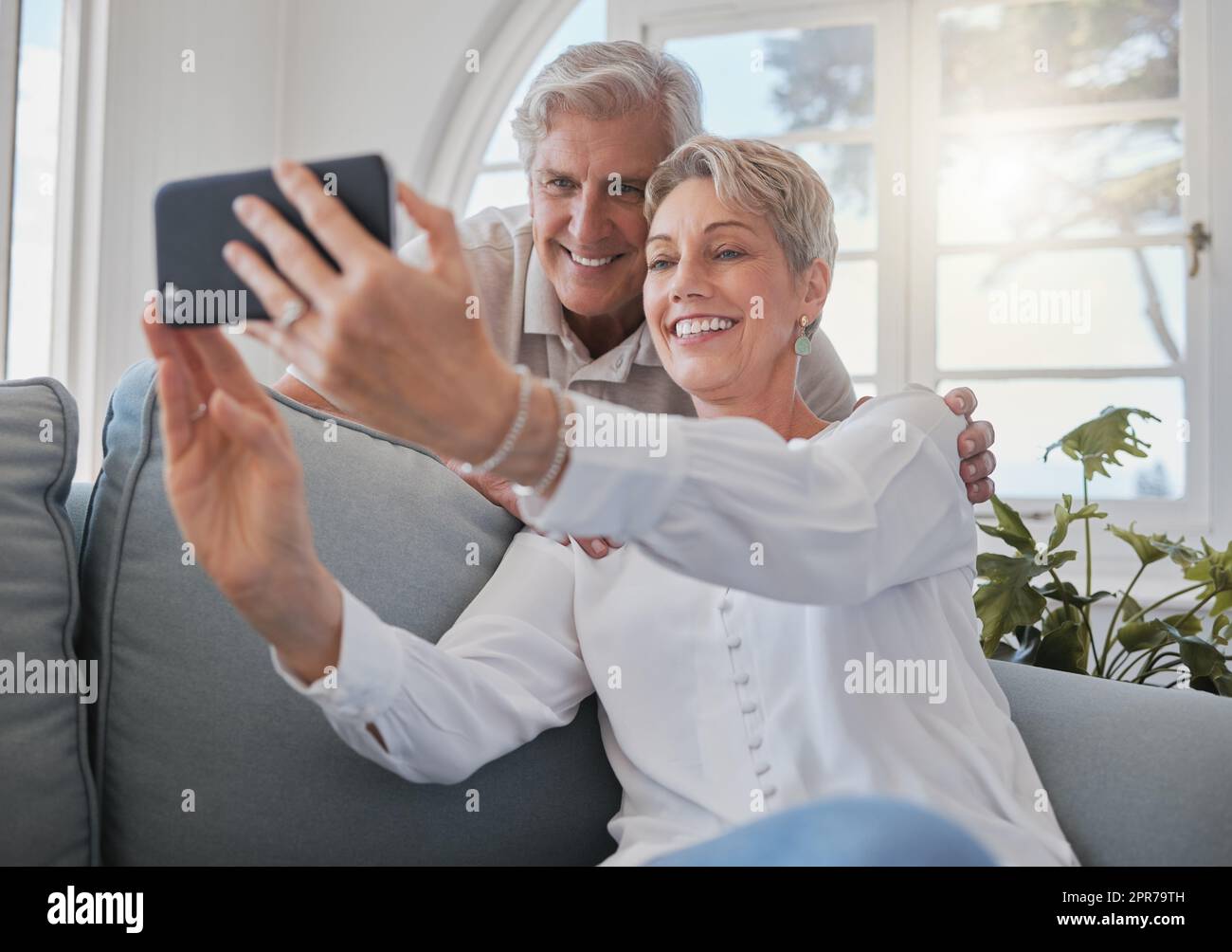 Un couple affectueux et expérimenté qui prend ses selfies tout en se relaxant dans le salon de la maison. Banque D'Images