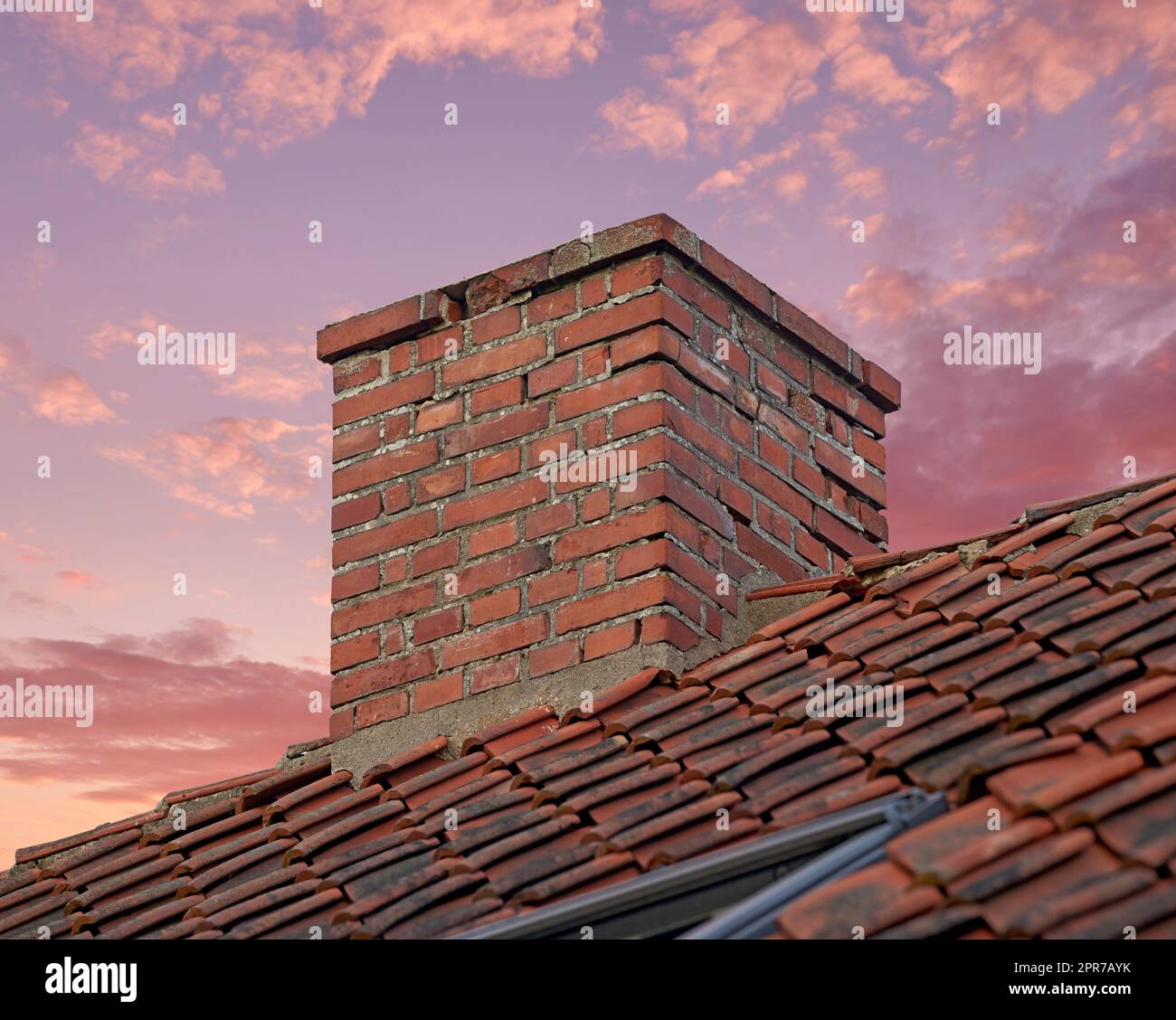 Gros plan d'une cheminée en briques rouges contre un ciel de coucher de soleil coloré pour les gaz de combustion et l'isolation de la maison sur le toit carrelé. Conception architecturale sur le bâtiment de la maison pour l'extraction de fumée de la cheminée ou du four Banque D'Images