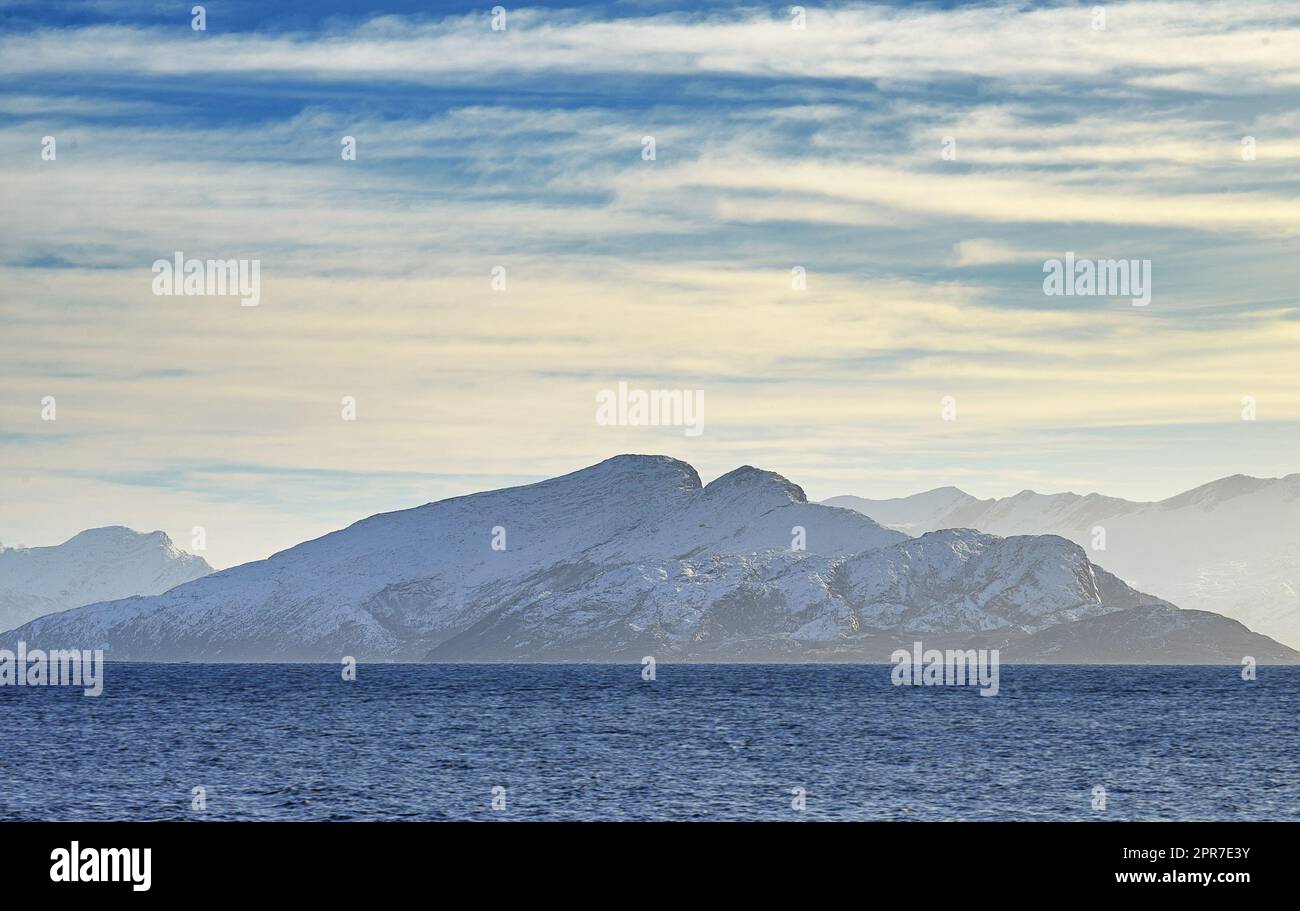 Vue panoramique sur les montagnes enneigées le long d'une côte à Bodo, Norvège. Vue naturelle sur un lac au lever du soleil le matin. Végétation luxuriante et isolée le long d'un lac dans une destination européenne Banque D'Images