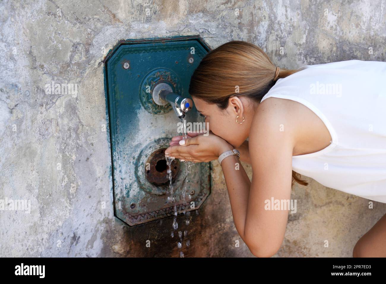 La jeune femme s'hydrate d'une fontaine lors d'une vague de chaleur dans la ville Banque D'Images