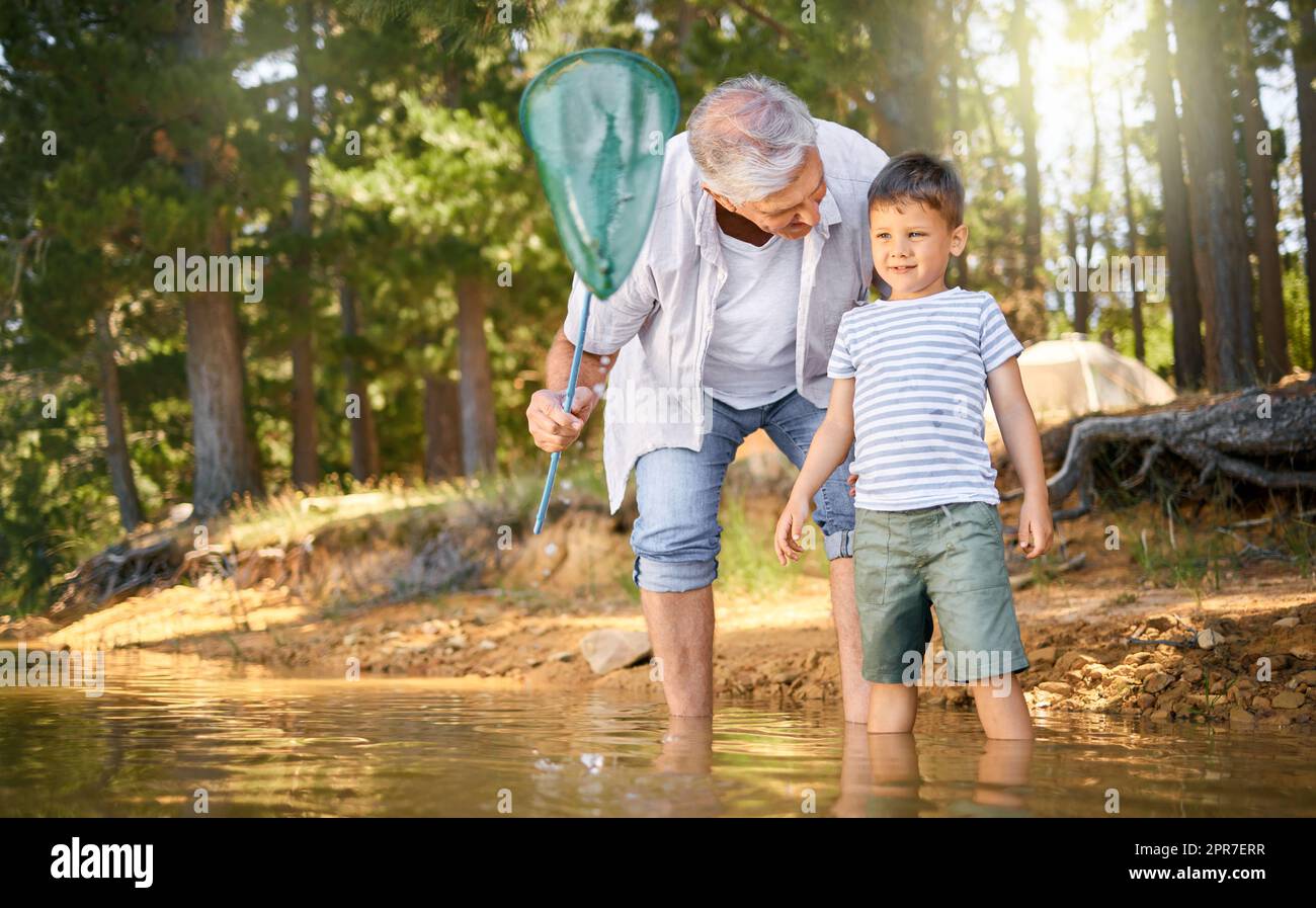 HES toujours prêt pour une aventure. Photo d'un petit garçon et de son grand-père pêchant avec un filet au lac dans une forêt. Banque D'Images
