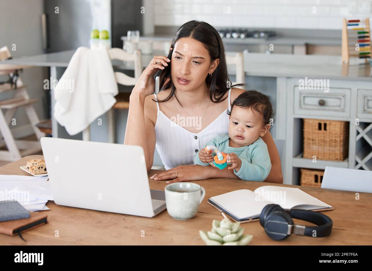 Les mamans sont les plus proches des super-héros. Photo d'une femme parlant sur son téléphone portable tout en étant assise avec son ordinateur portable et son bébé sur ses genoux. Banque D'Images