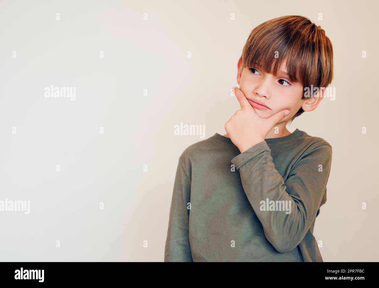 Des ombres qui se jettent dans les yeux. Studio photo d'un petit garçon mignon perdu dans ses pensées en posant contre un mur. Banque D'Images