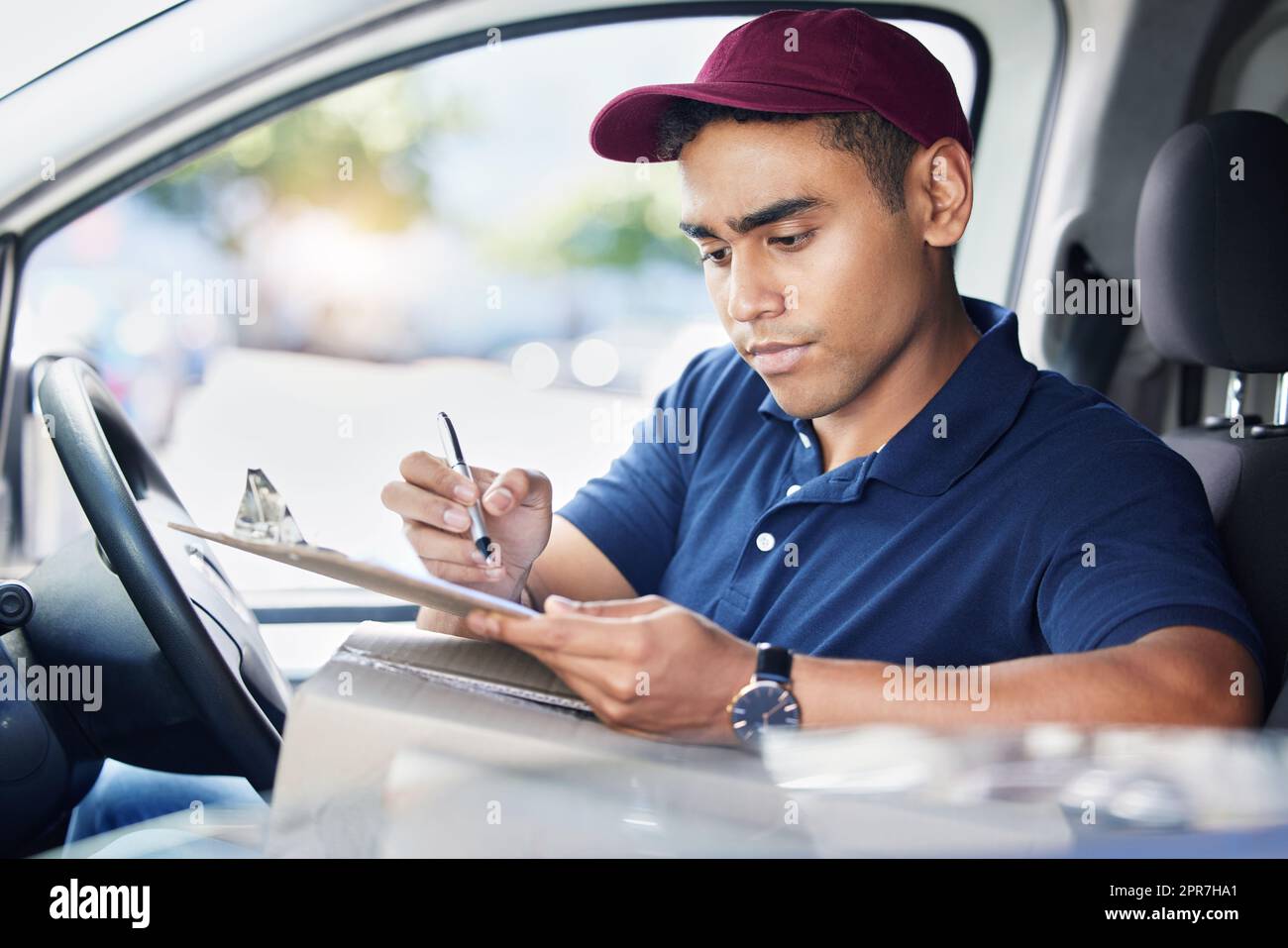 Planifier son itinéraire de livraison pour la journée. Un jeune liveur écrit sur une planchette à pince tout en étant assis dans une camionnette. Banque D'Images