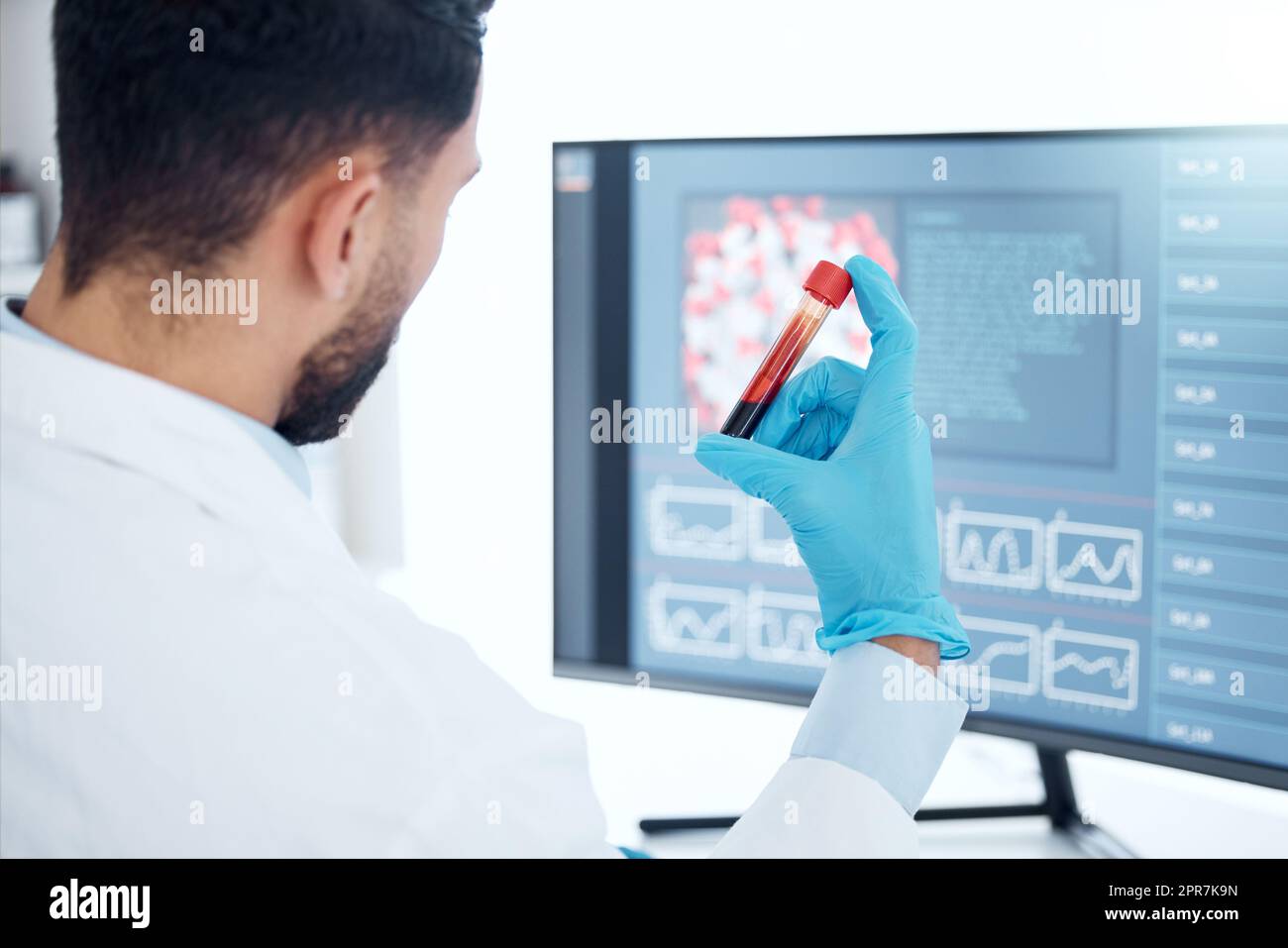 Scientifique médical inconnu de race mixte assis seul dans un laboratoire, tenant un flacon de sang et utilisant un ordinateur pour l'examiner. Professionnel de la santé hispanique analysant un échantillon de tube à essai en clinique Banque D'Images