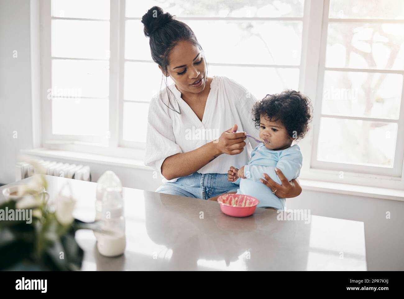 Vous devez manger. A tourné une jeune femme attrayante assise dans la cuisine avec sa fille et la nourrissant. Banque D'Images