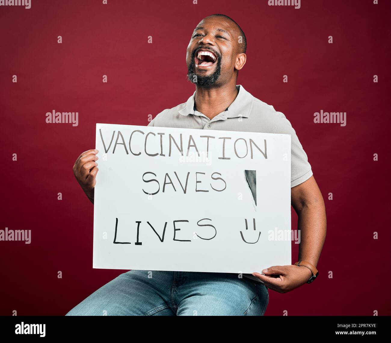 Homme vacciné covid afro-américain montrant et tenant une affiche. Criant homme noir isolé sur fond rouge studio avec espace de copie. Modèle excité avec signe pour promouvoir le vaccin corona et motiver Banque D'Images
