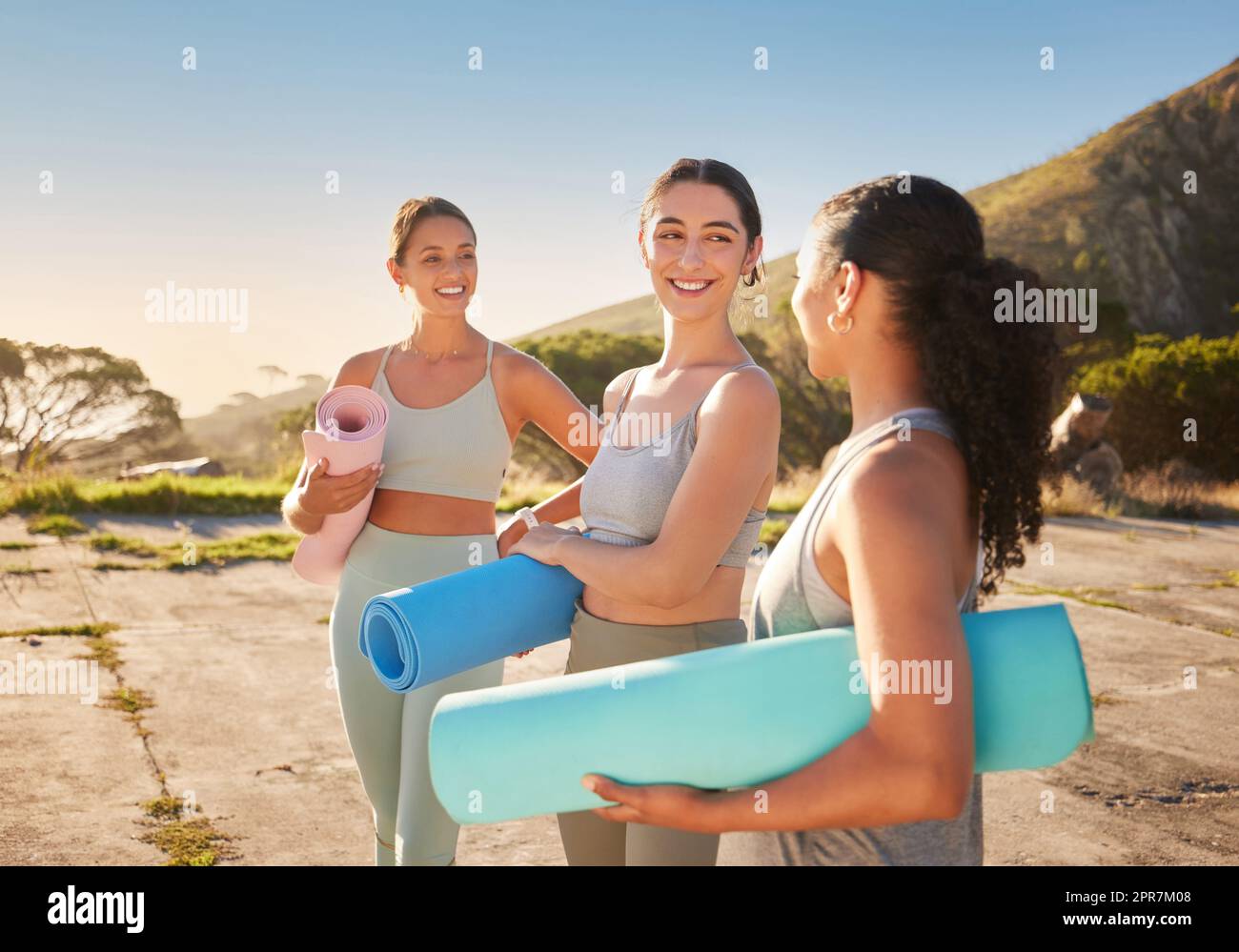 Belles femmes de yoga liant et tenant des tapis de yoga dans la pratique en plein air dans la nature éloignée. Groupe diversifié de jeunes amis actifs souriants debout ensemble. Trois personnes heureuses se préparent à être conscientes Banque D'Images