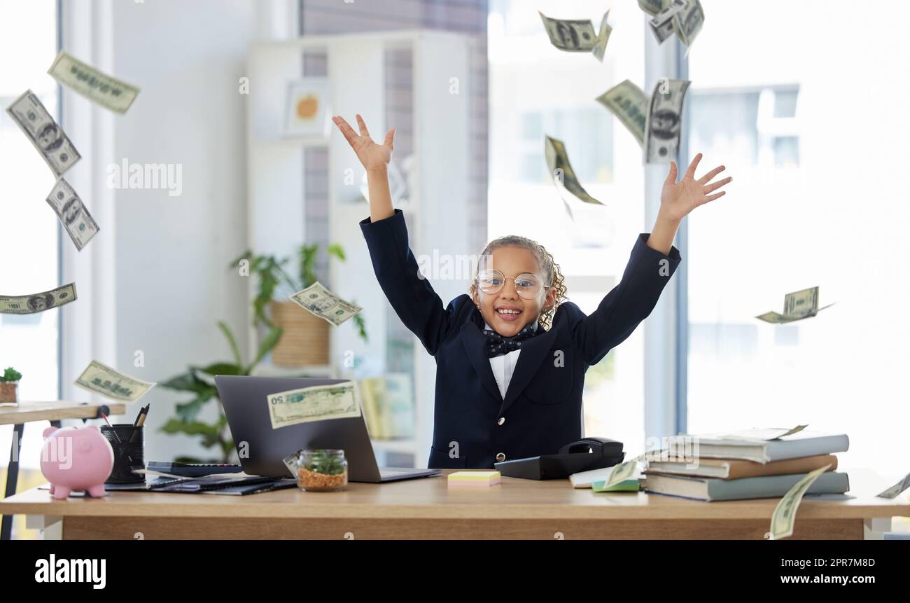 Il pleut de l'argent. Une adorable petite fille habillée comme une femme d'affaires assise seule dans un bureau et jetant de l'argent. Banque D'Images