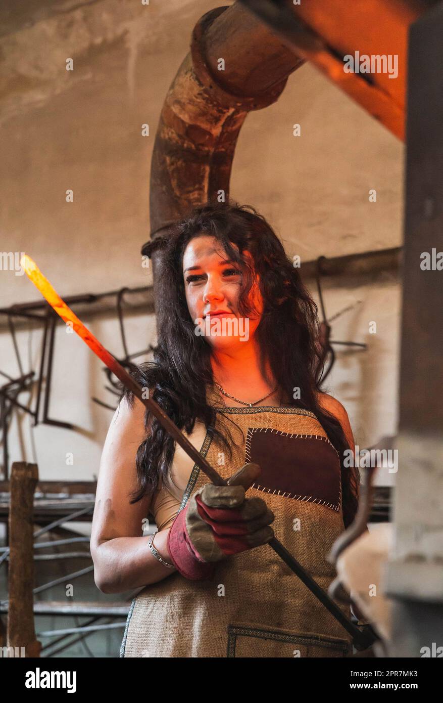 le forgeron tient une tige métallique rouge-chaude dans l'atelier Banque D'Images