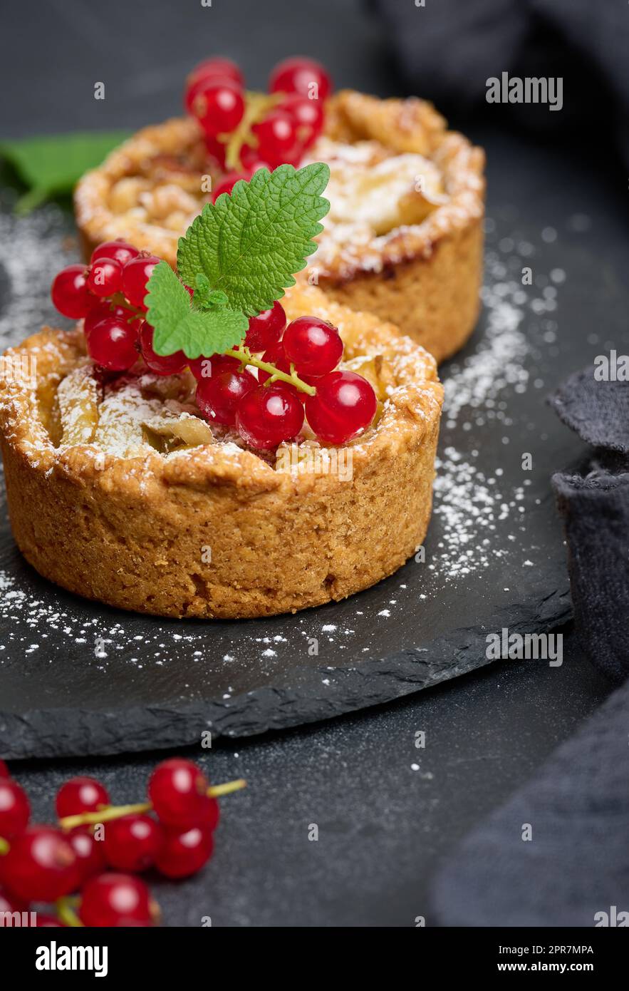 Tarte aux fruits avec des raisins de Corinthe rouges saupoudrés de sucre sur une table noire, délicieux dessert Banque D'Images