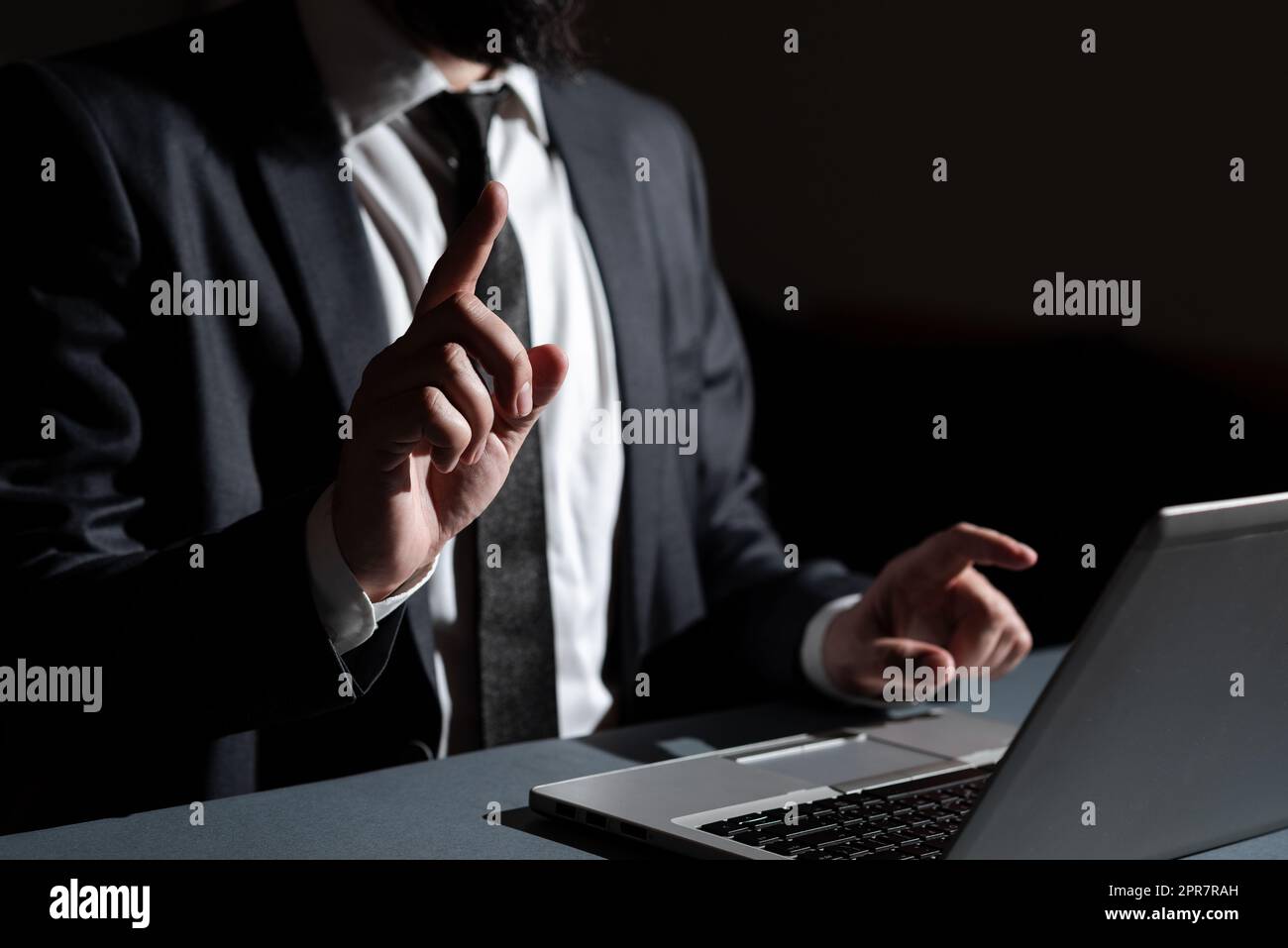Homme d'affaires pointant avec deux doigts sur des informations importantes assis sur un bureau avec un ordinateur portable. Homme en costume présentant des messages essentiels avec les deux mains. Exécutif montrant les données. Banque D'Images