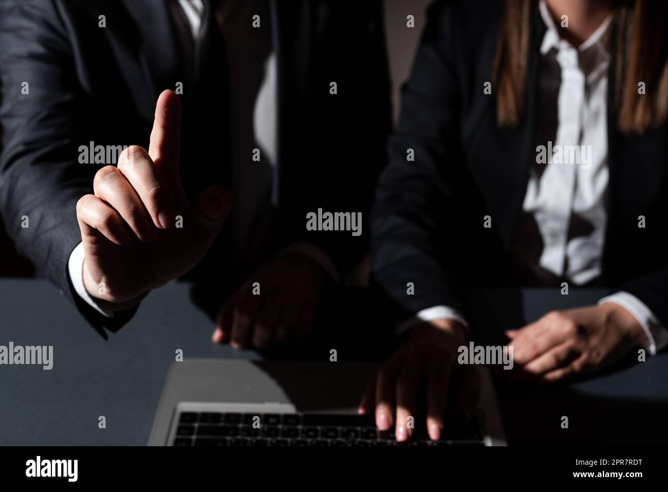 Femme assise sur un bureau avec un ordinateur portable et un homme pointant d'un doigt sur des messages importants. Homme d'affaires présentant des informations crutiales d'une main. Banque D'Images