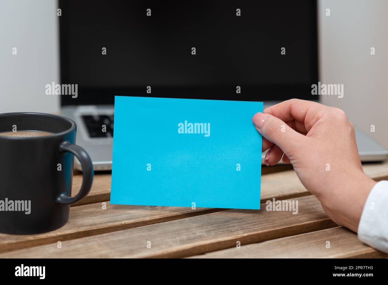 Femme d'affaires tenant une note avec un message important sur la table avec un plateau et un café. Femme présentant des informations sur le papier sur le bureau avec ordinateur et la tasse. Banque D'Images