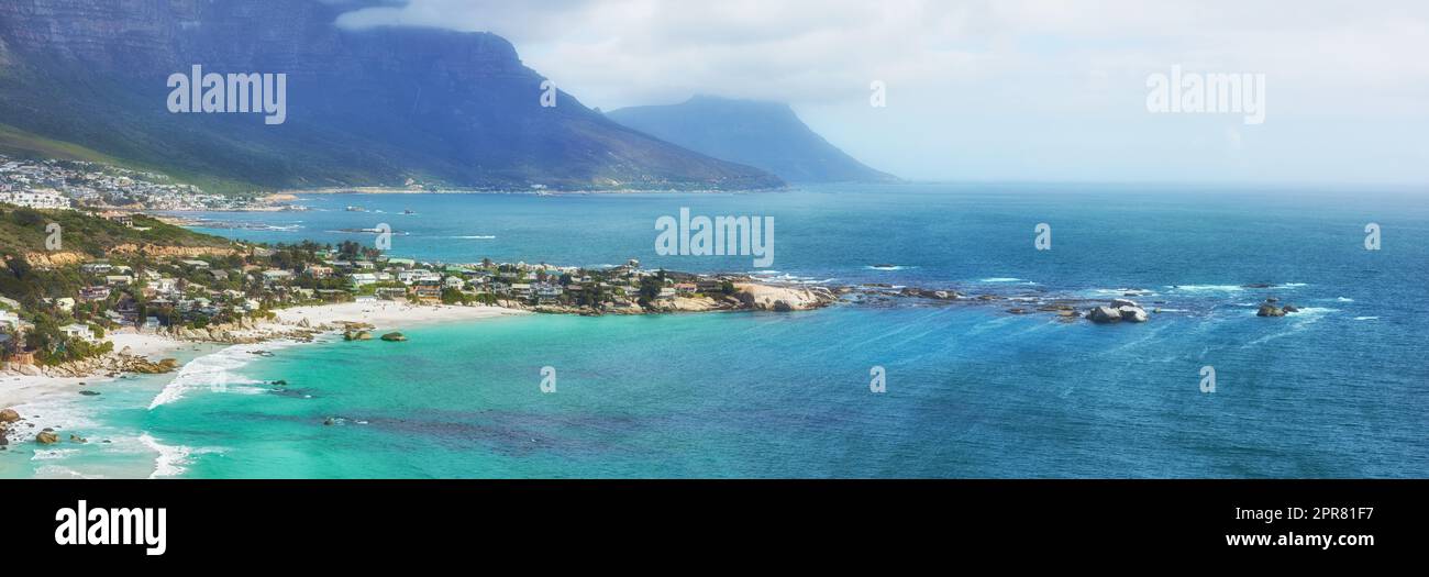 Une vue paisible sur l'océan Clifton au bord de l'Atlantique avec une île et des montagnes en arrière-plan. Une ville entourée d'eau douce bleue et d'un ciel brumeux et nuageux avec espace de copie. Banque D'Images
