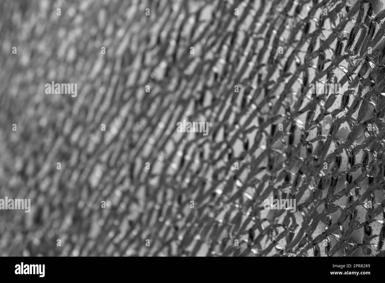 Gros plan monochromatique d'un verre de sécurité feuilleté fissuré avec un foyer sur le côté droit et un flou de fondu sur la gauche, créant une texture abstraite. Banque D'Images