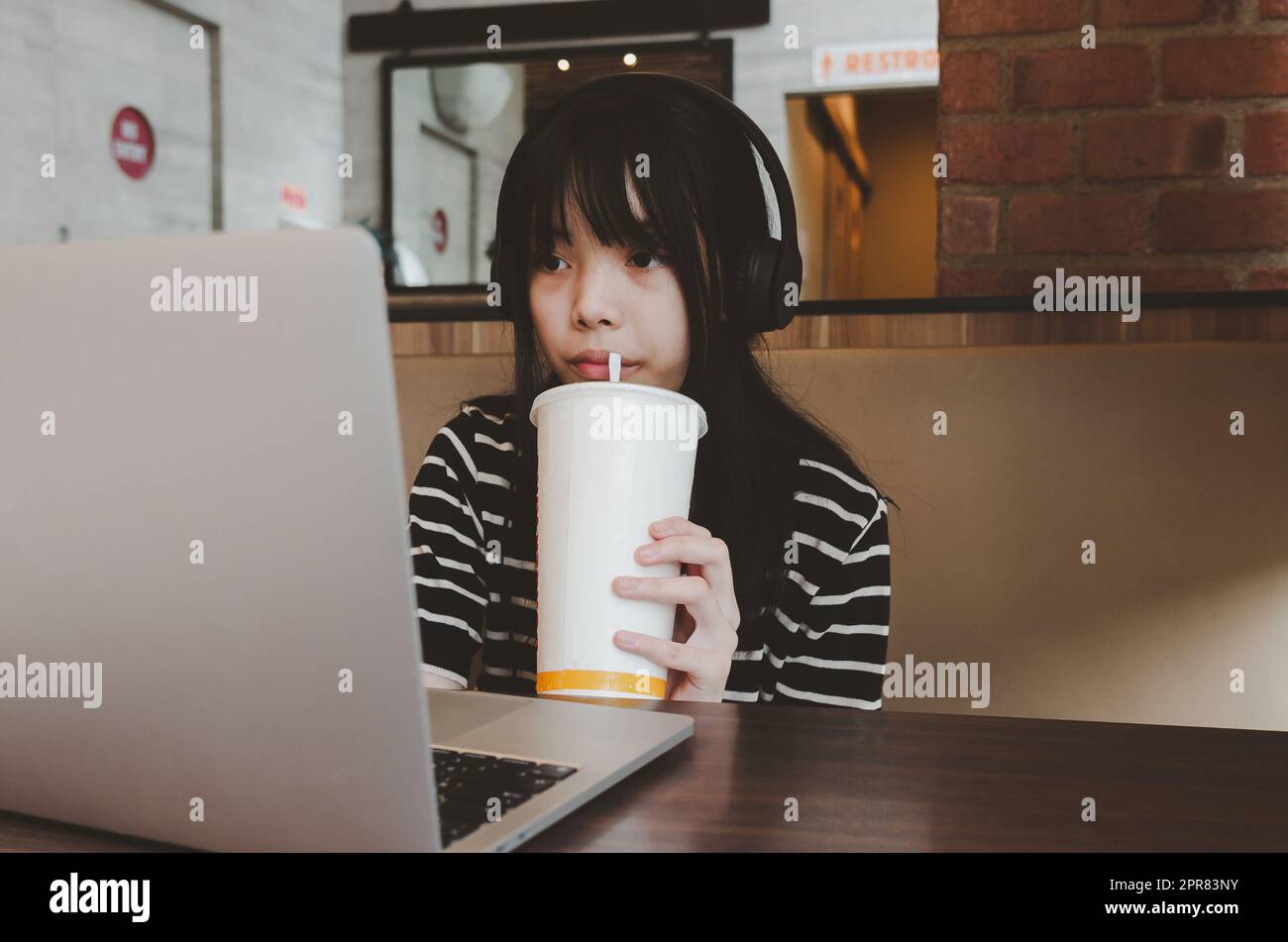 Les adolescentes portent un casque pour regarder des films sur les réseaux sociaux ou étudier en ligne en buvant de l'eau et en se relaxant sur le canapé. Banque D'Images