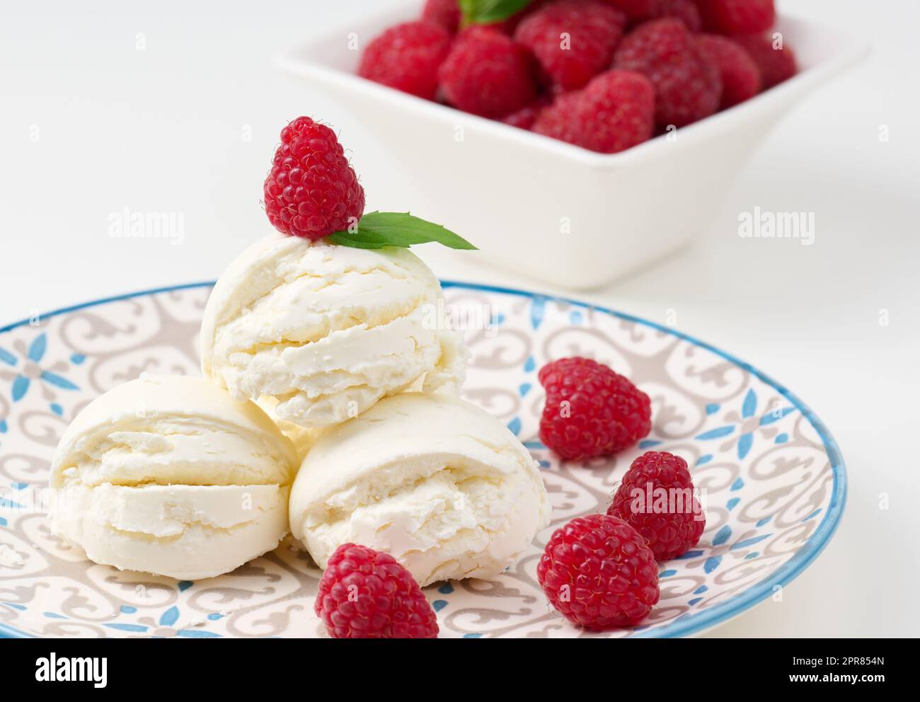 Boules de glace à la vanille aux framboises rouges dans une assiette ronde Banque D'Images