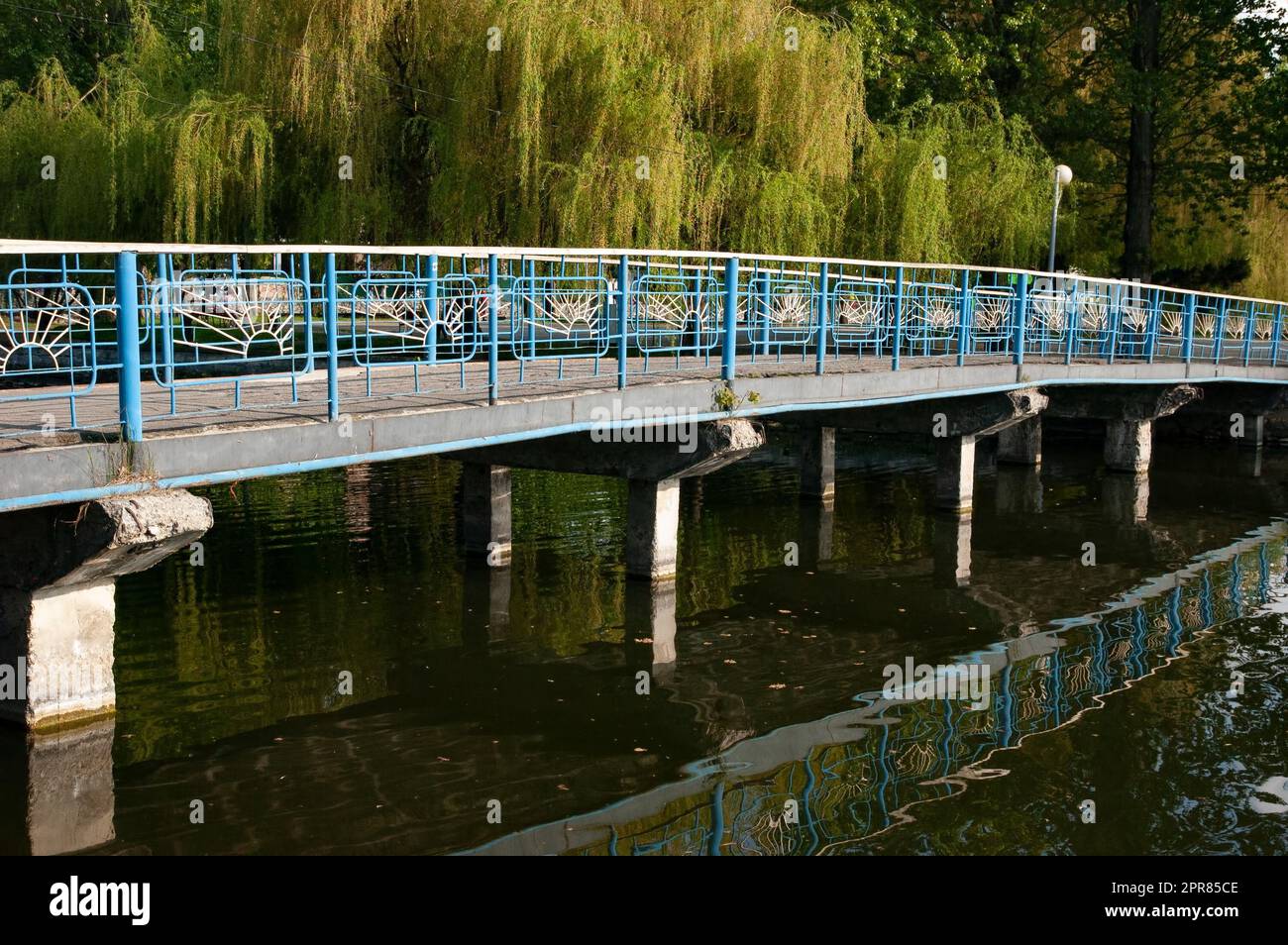 un pont avec des rampes est jeté au-dessus de l'eau verte, sur le rivage les saules sont penchées au-dessus de l'eau. Banque D'Images